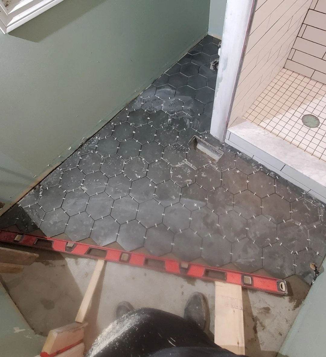 Installing hexagon black tiles in a bathroom shower area, with spacers and construction tools visible.
