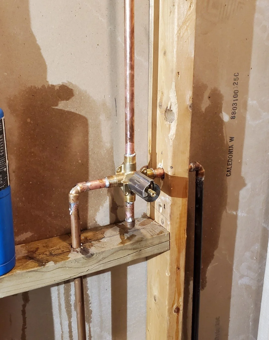 Copper plumbing pipes and fittings installed on a wooden wall in a construction area.