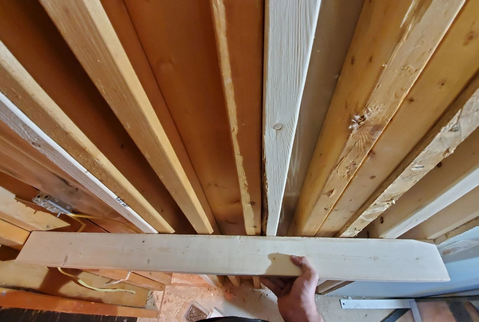 Person holding a piece of wood framing in an unfinished wall with multiple wooden studs and electrical wiring.
