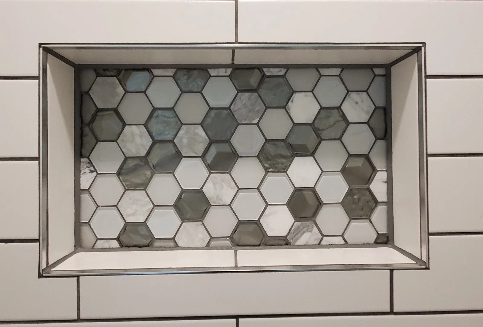 Close-up of a shower niche with white and gray hexagonal marble tiles.
