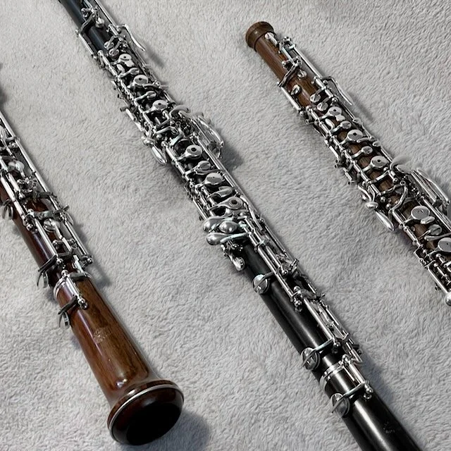 Three oboes, angled, lying on a gray carpeted surface.