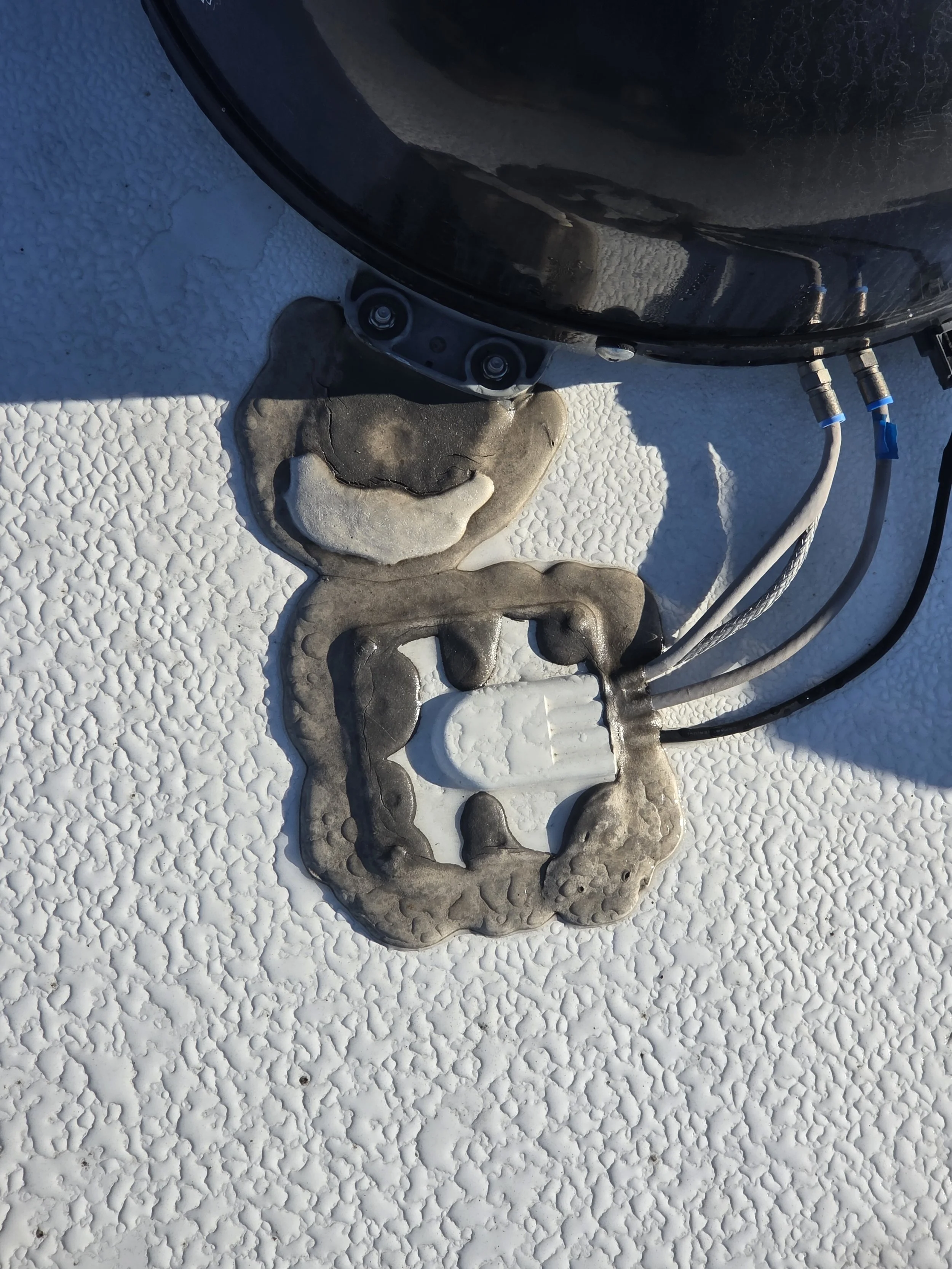 Close-up of a black cylindrical object with cables attached, mounted on a textured white surface with peeling paint and rubber sealant underneath.