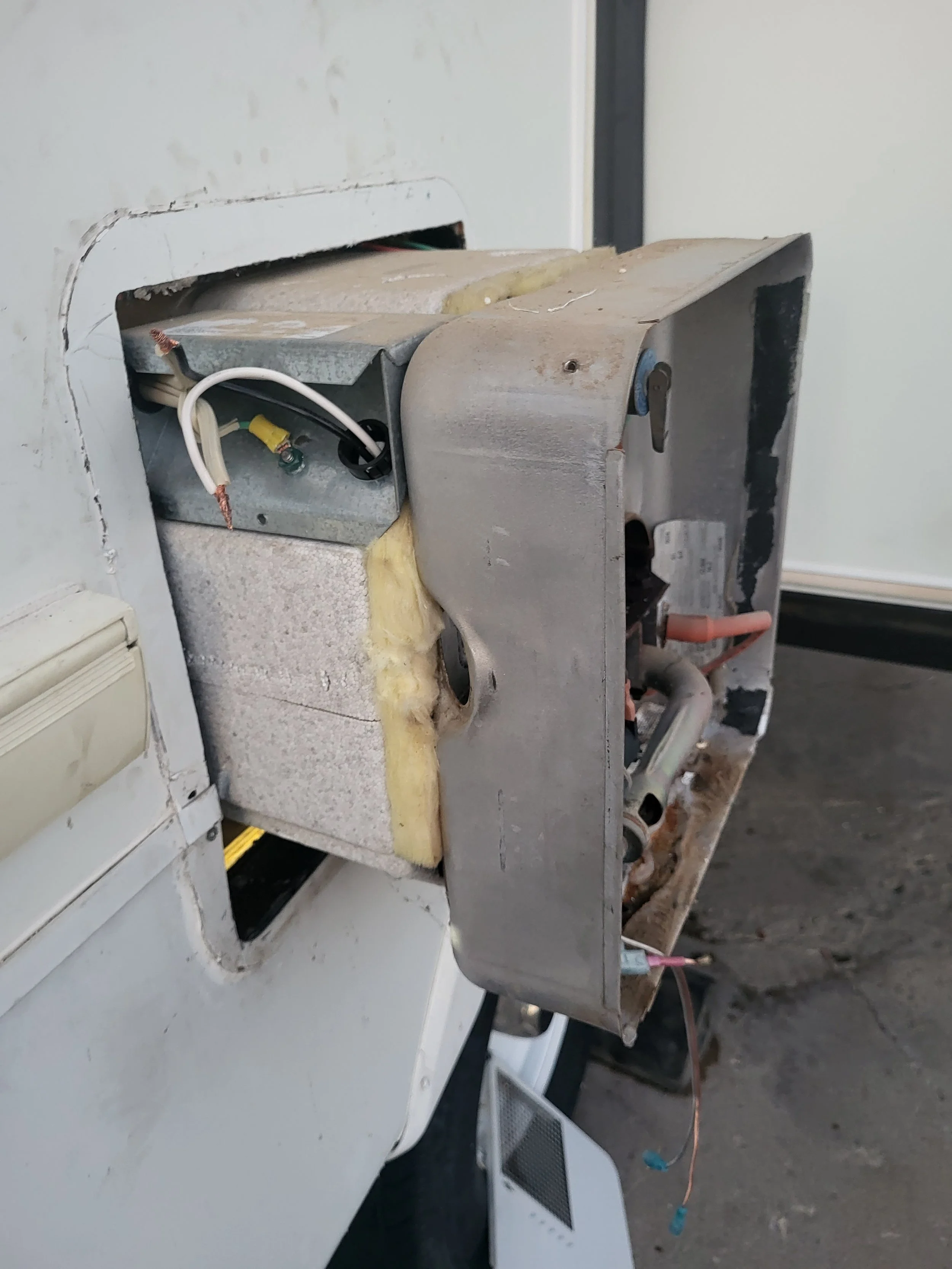 Open front panel of broken or faulty washing machine, showing internal metal components, wires, and insulation.