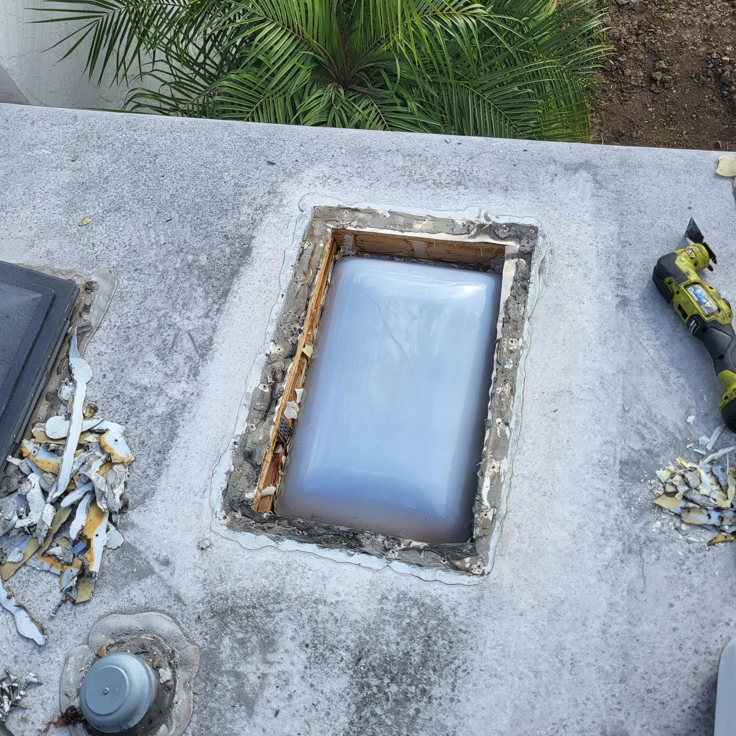 Rooftop with a skylight window being replaced or repaired, with tools and debris around.