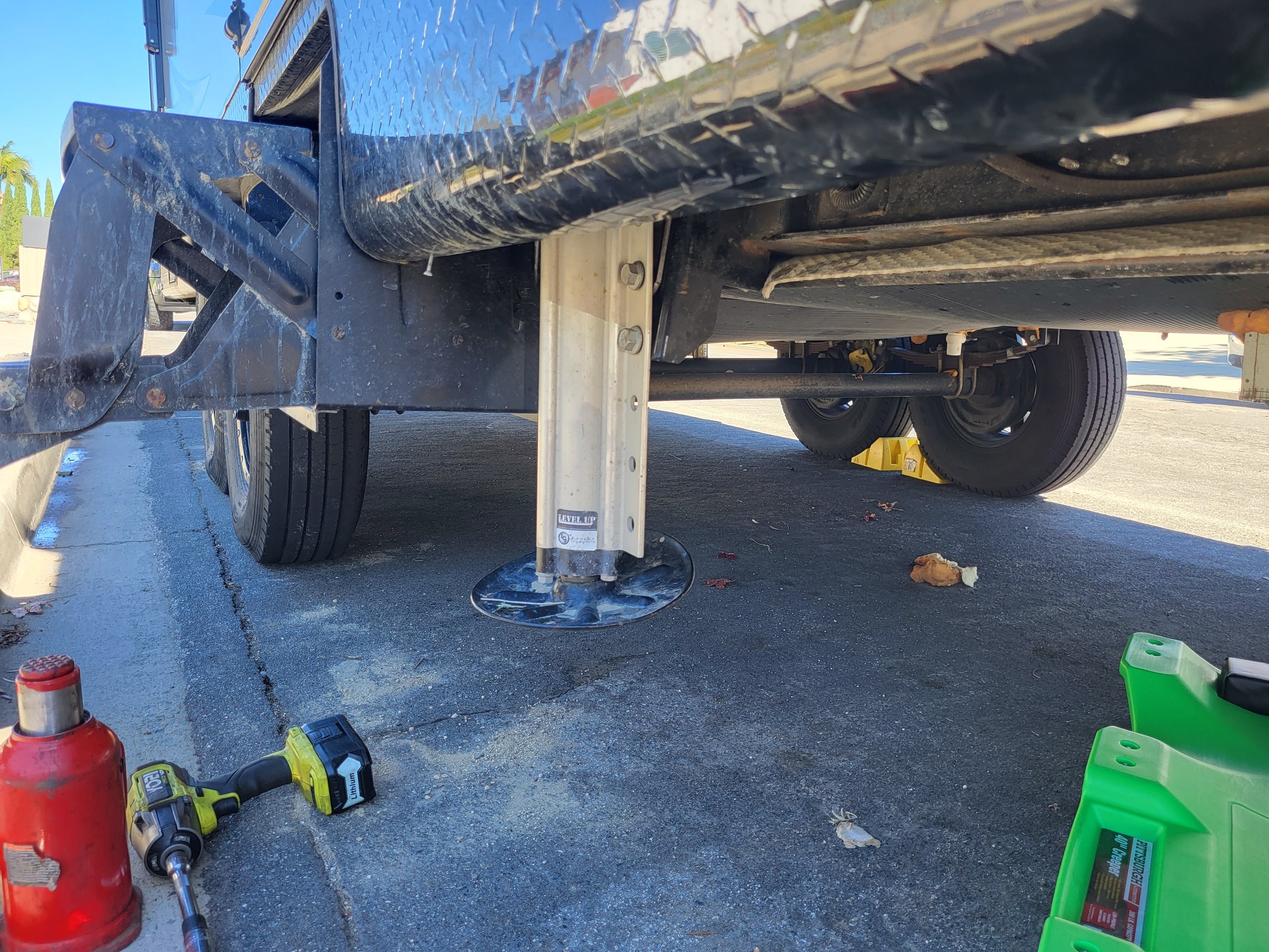 Close-up of a boat trailer support leg with tools and equipment nearby on a paved surface.