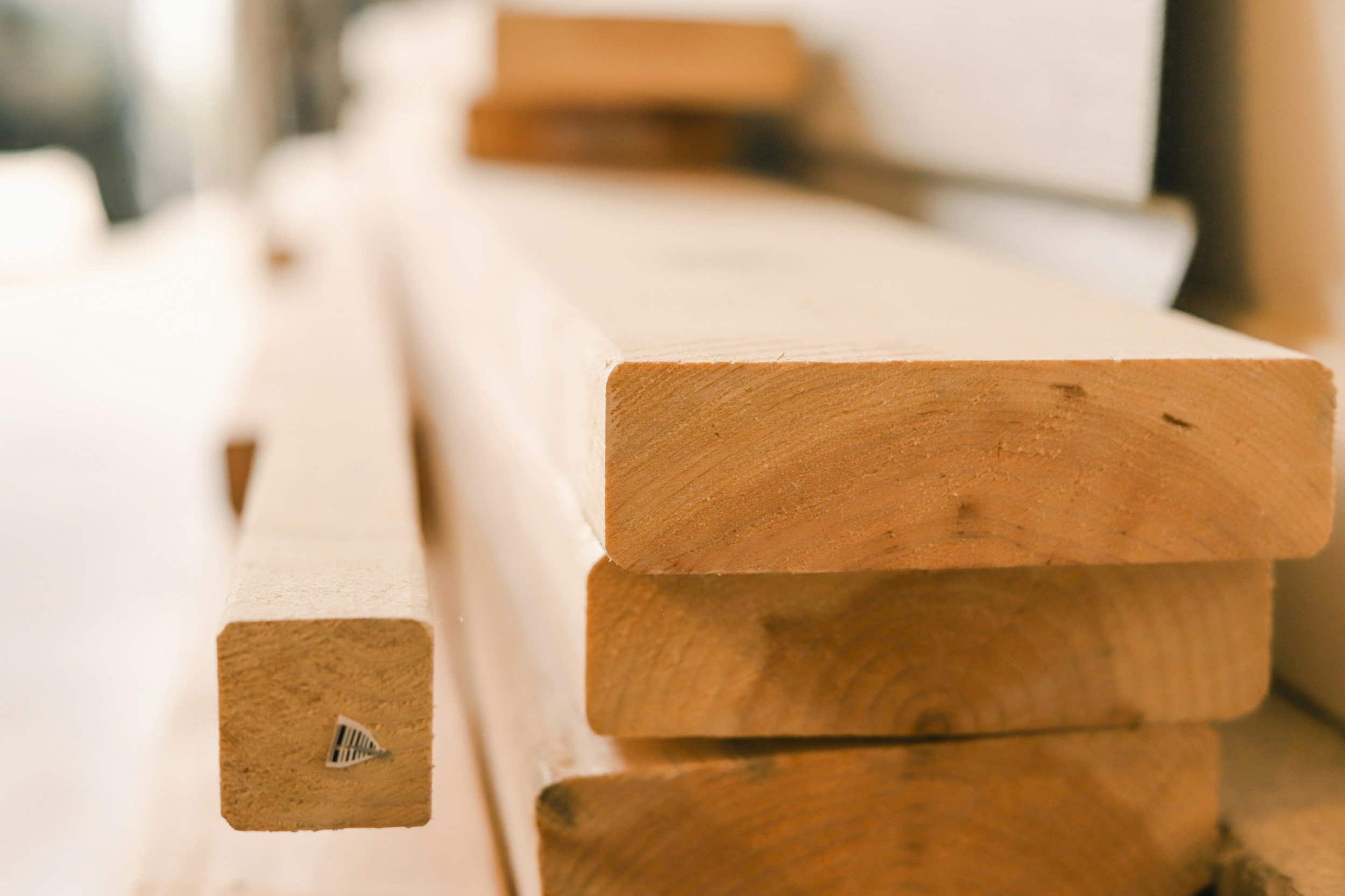 Close-up of stacked wooden planks with smooth surfaces and visible wood grain. The focus is on the edge of the planks, with the background slightly blurred.