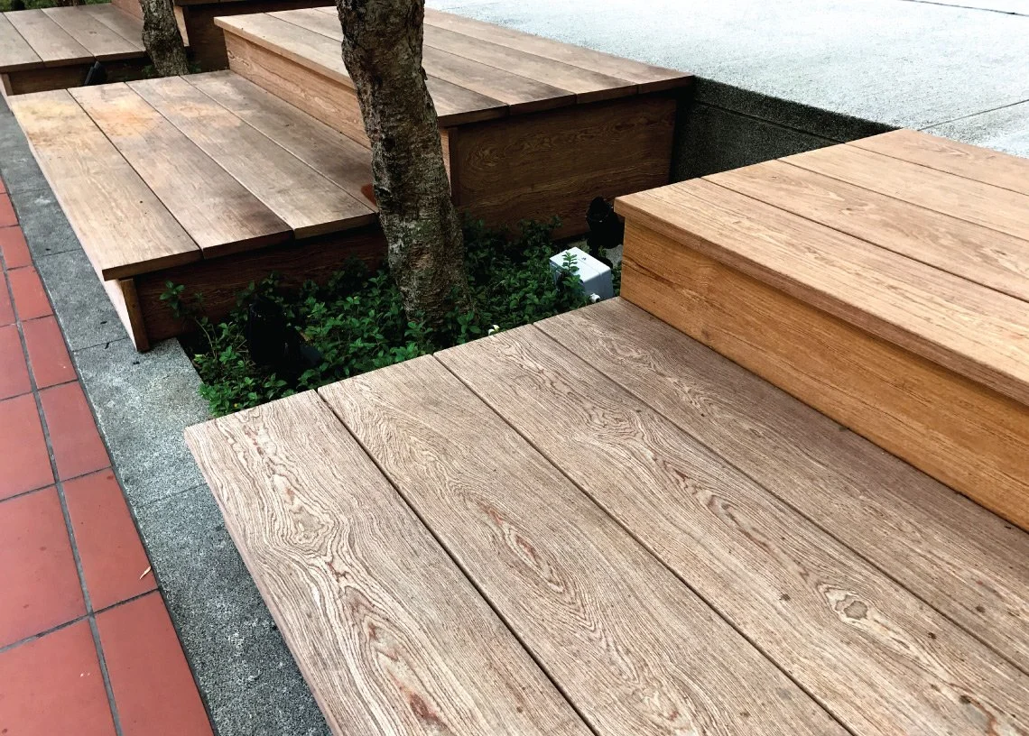 Wooden benches surrounding a small tree planted in a garden bed next to a sidewalk.