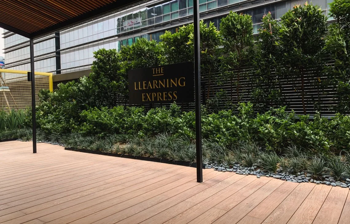 Outdoor area with wooden deck, green bushes, and a black sign that reads "The Learning Express" in gold letters.