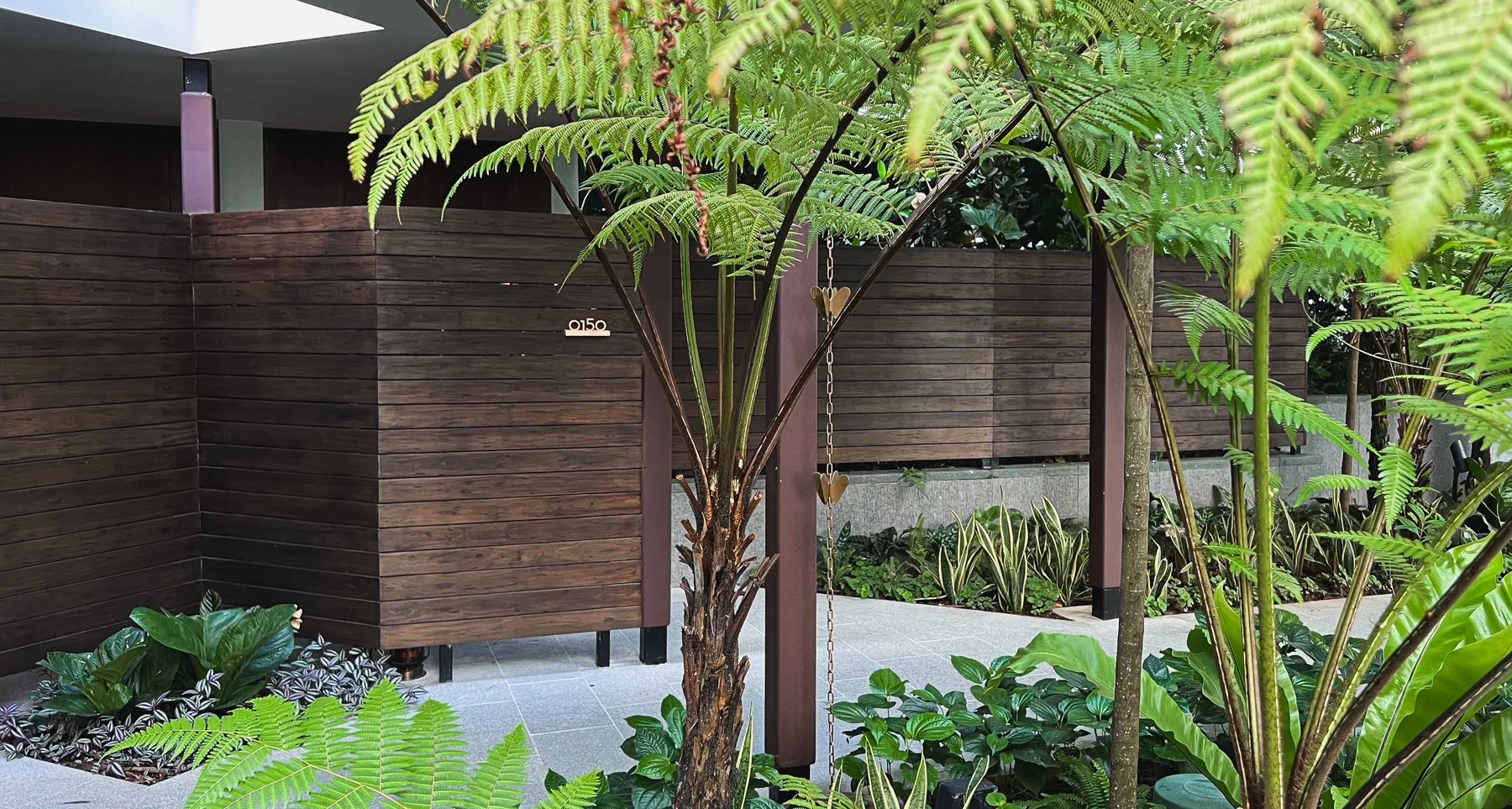 A modern outdoor area with wooden fencing, lush green plants, and a decorative chain with small hearts hanging from a tree.