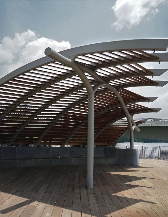 Modern architectural structure with curved wooden and metal beams, situated on a wooden deck outdoors.