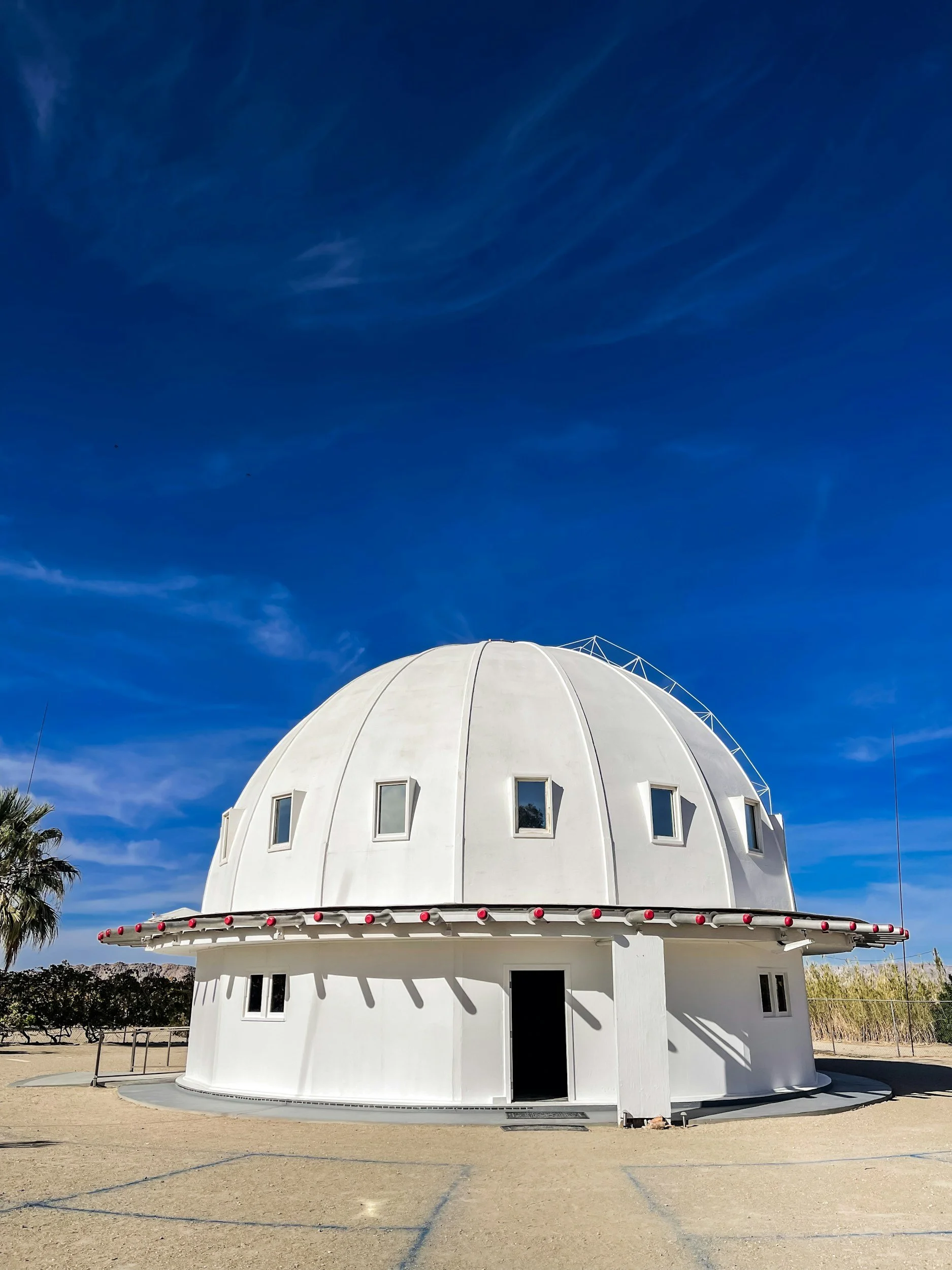 A white dome-shaped building with small windows and a central entrance, set against a bright blue sky.