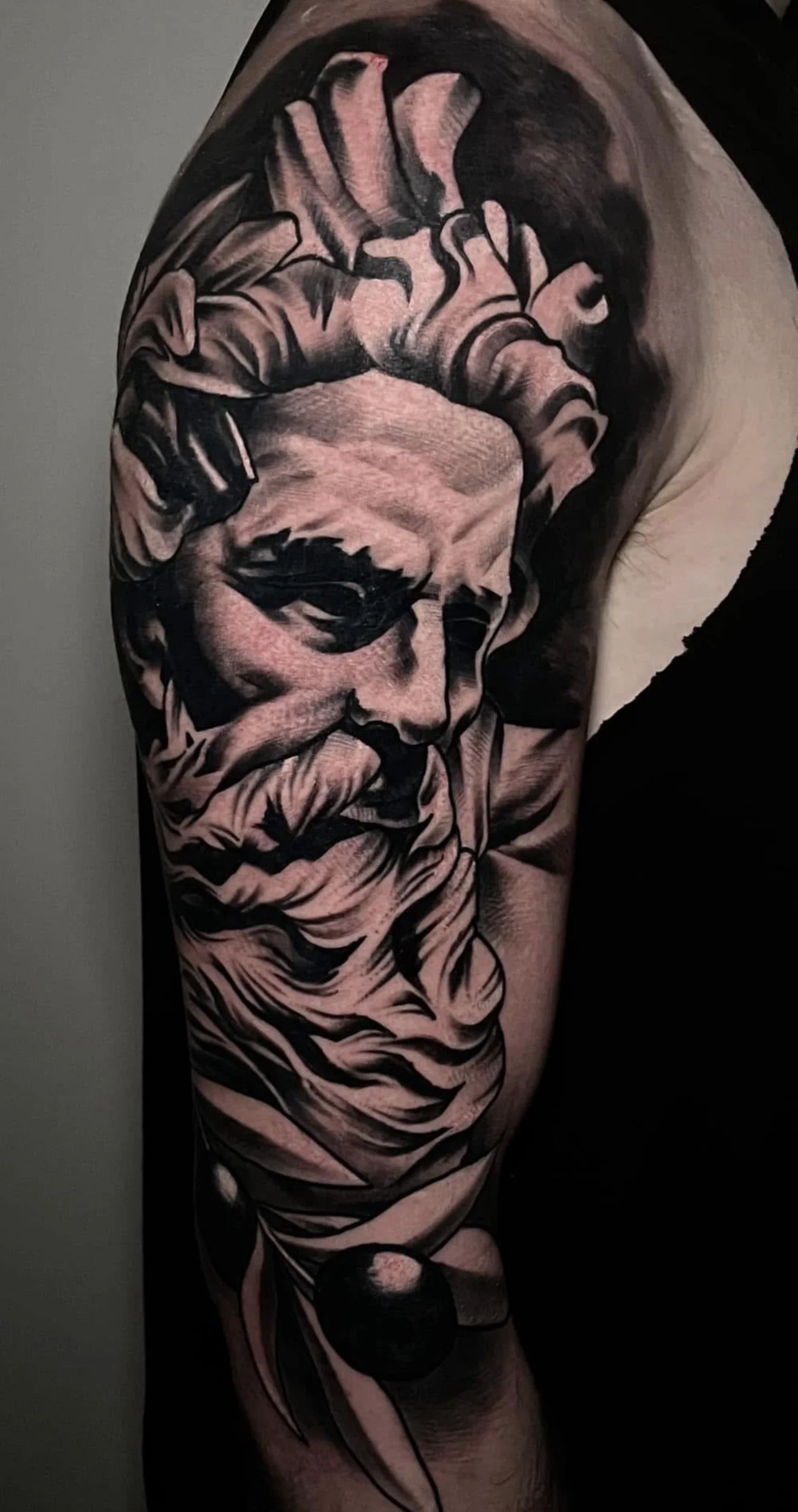 Black and grey tattoo of a classical statue face with flowing hair and beard, completed by Cody Eckenrode at CREate Tattoo Studio.