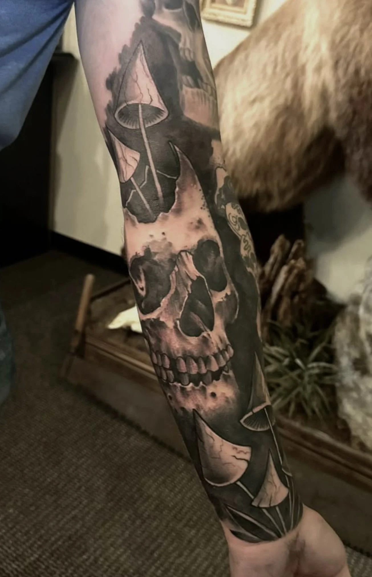 A detailed black and gray tattoo of a human skull with mushrooms growing out of it, covering most of the person's arm done by Cody Eckenrode at CREate Tattoo Studio.