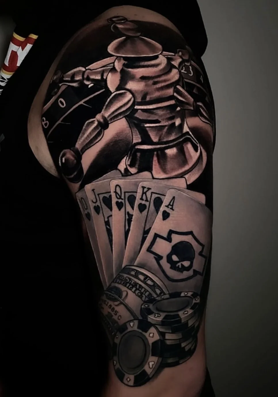 Casino-themed black and grey tattoo on upper arm with playing cards, poker chips, and a roulette wheel by Cody Eckenrode at CREate Tattoo Studio.