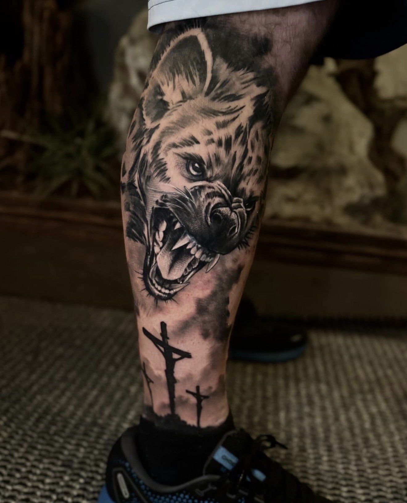 Detailed black and grey tattoo on the lower leg featuring a hyena positioned above a set of crosses, done by Cody Eckenrode at CREate Tattoo Studio.