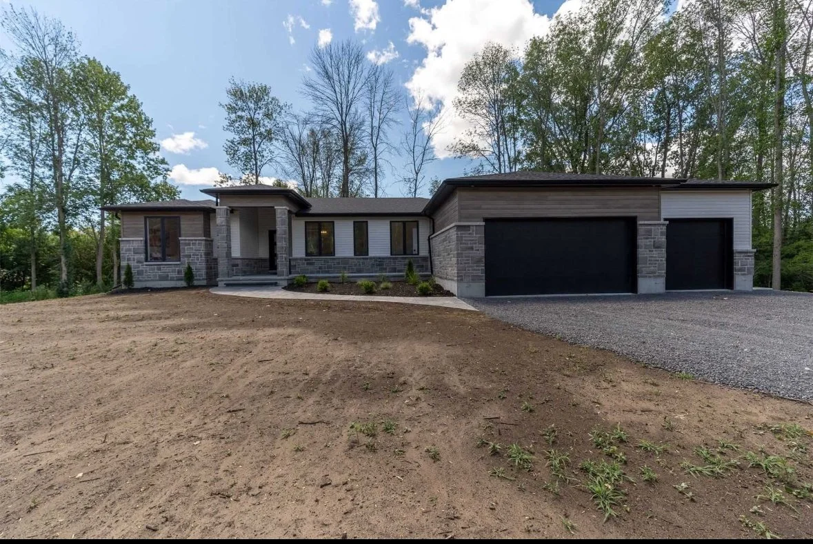 Newly constructed modern house with a front yard, driveway, and a two-car garage, surrounded by trees.
