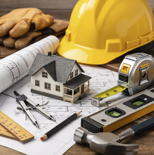 Construction tools and supplies on blueprints, including a yellow hard hat, miniature house model, measuring tape, hammer, ruler, compass, pencil, and gloves.