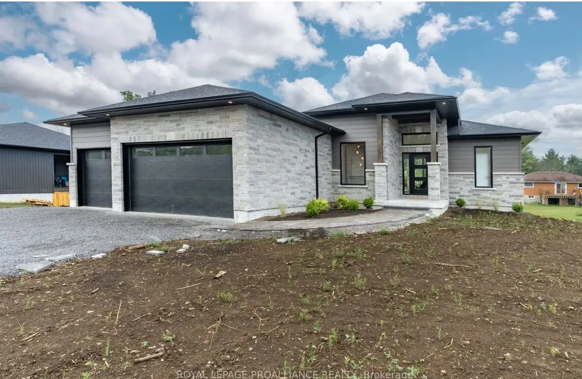 Modern house with gray brick and siding exterior, black garage doors, and a small front porch surrounded by new landscaping.