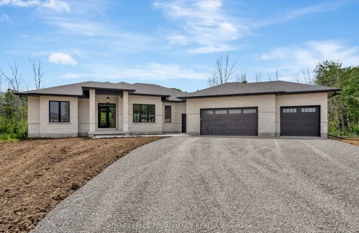 New modern house with a gravel driveway, brick exterior, black garage doors, and a front porch under a blue sky.