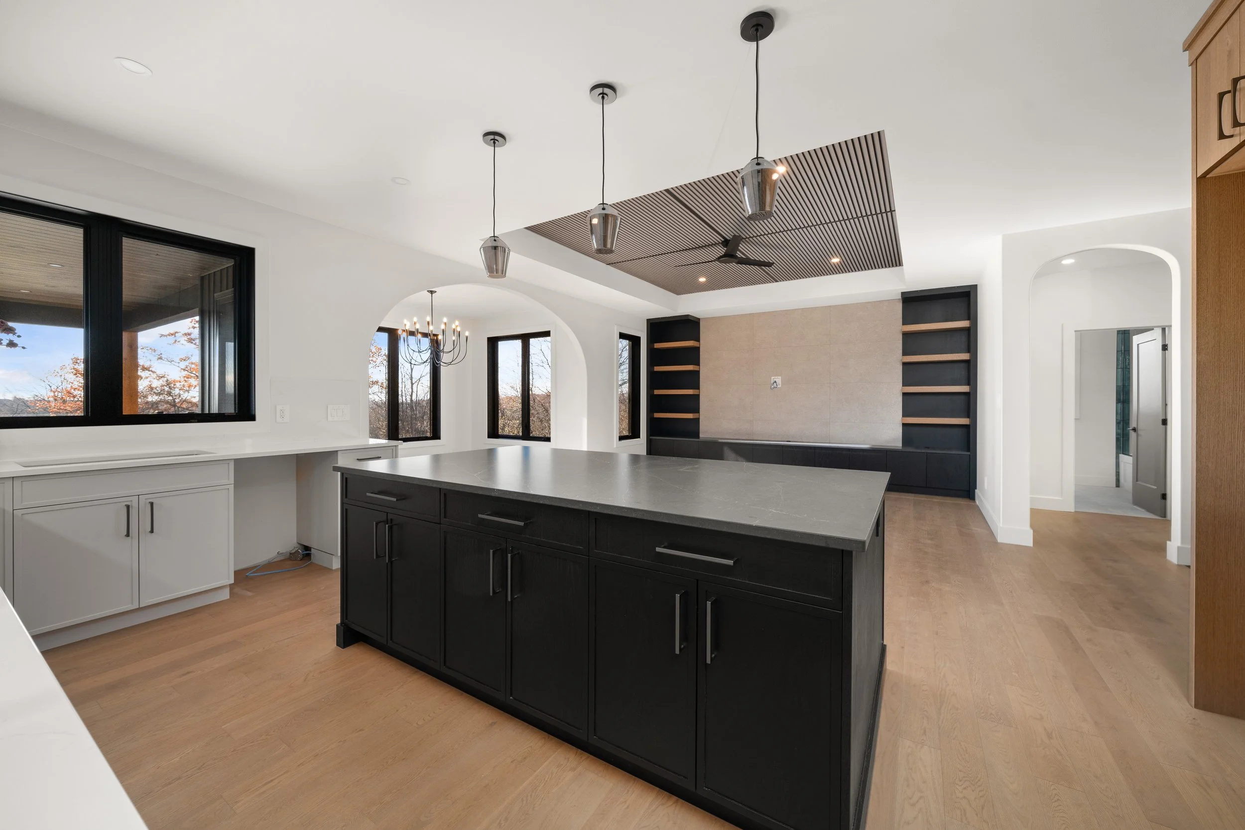 Modern kitchen with black island, white cabinets, light wooden flooring, and large windows.