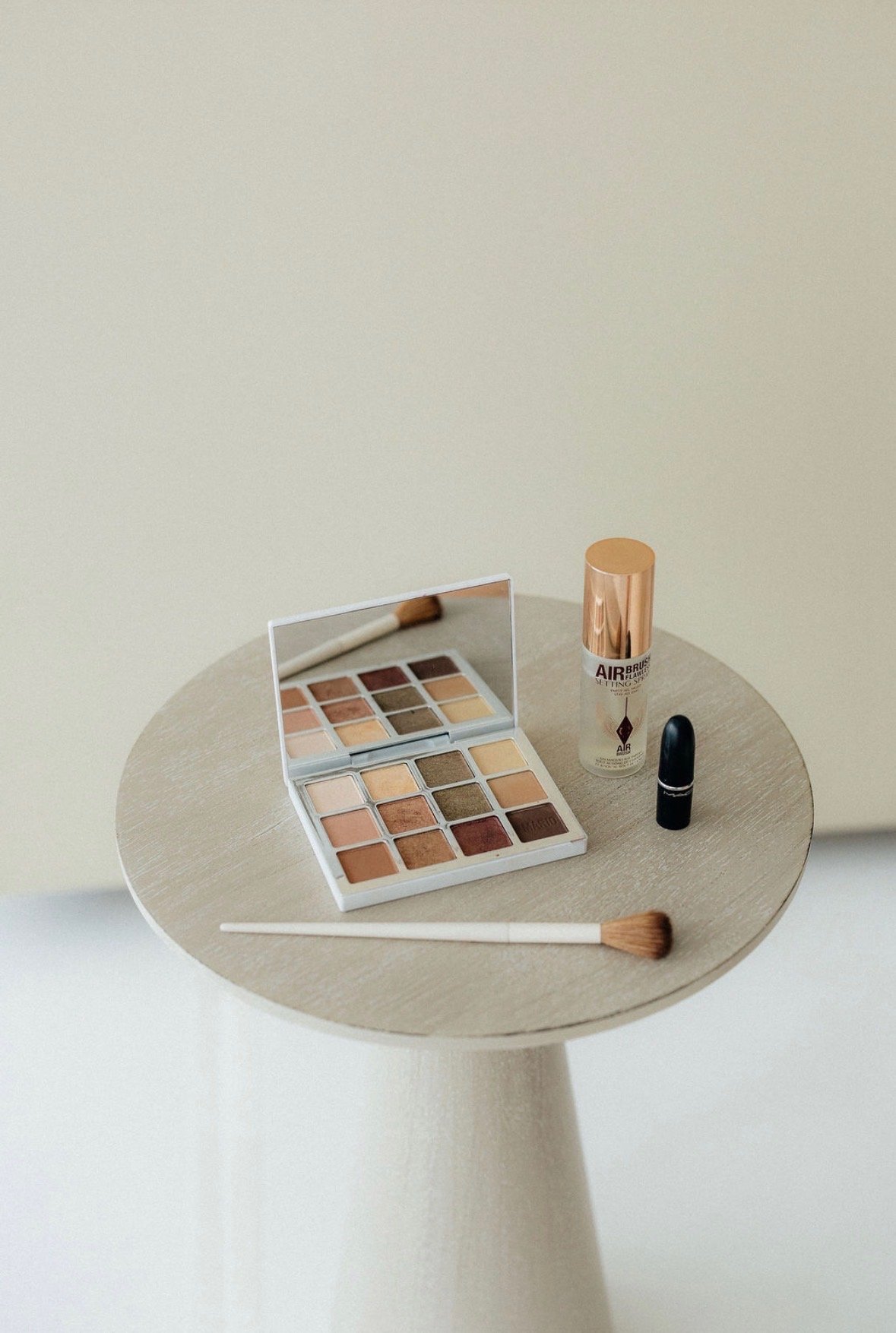 Bridal makeup products including foundation, lipstick and brushed styled on a neutral tabletop.
