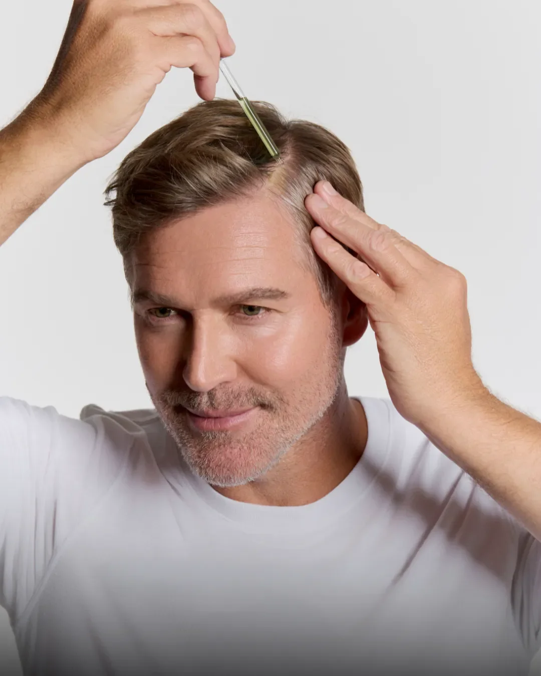 A middle-aged man with gray hair getting a hair treatment or injection in his scalp, with a healthcare professional using a syringe.