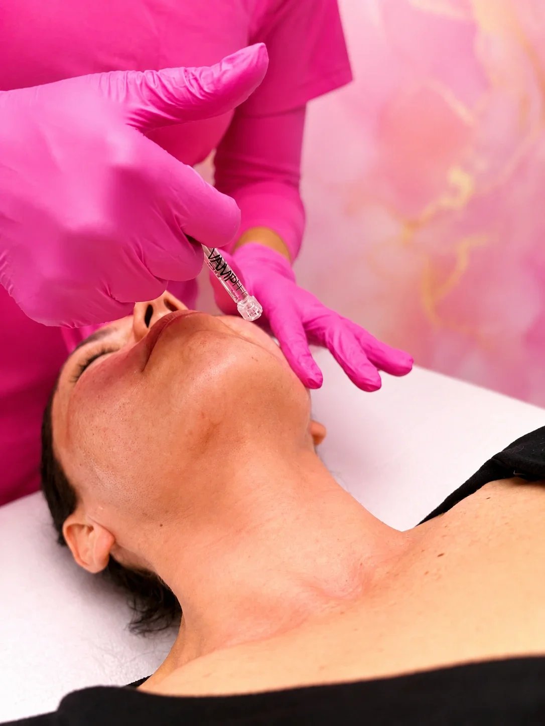 A person receiving an injection in their cheek from a medical professional wearing pink gloves.