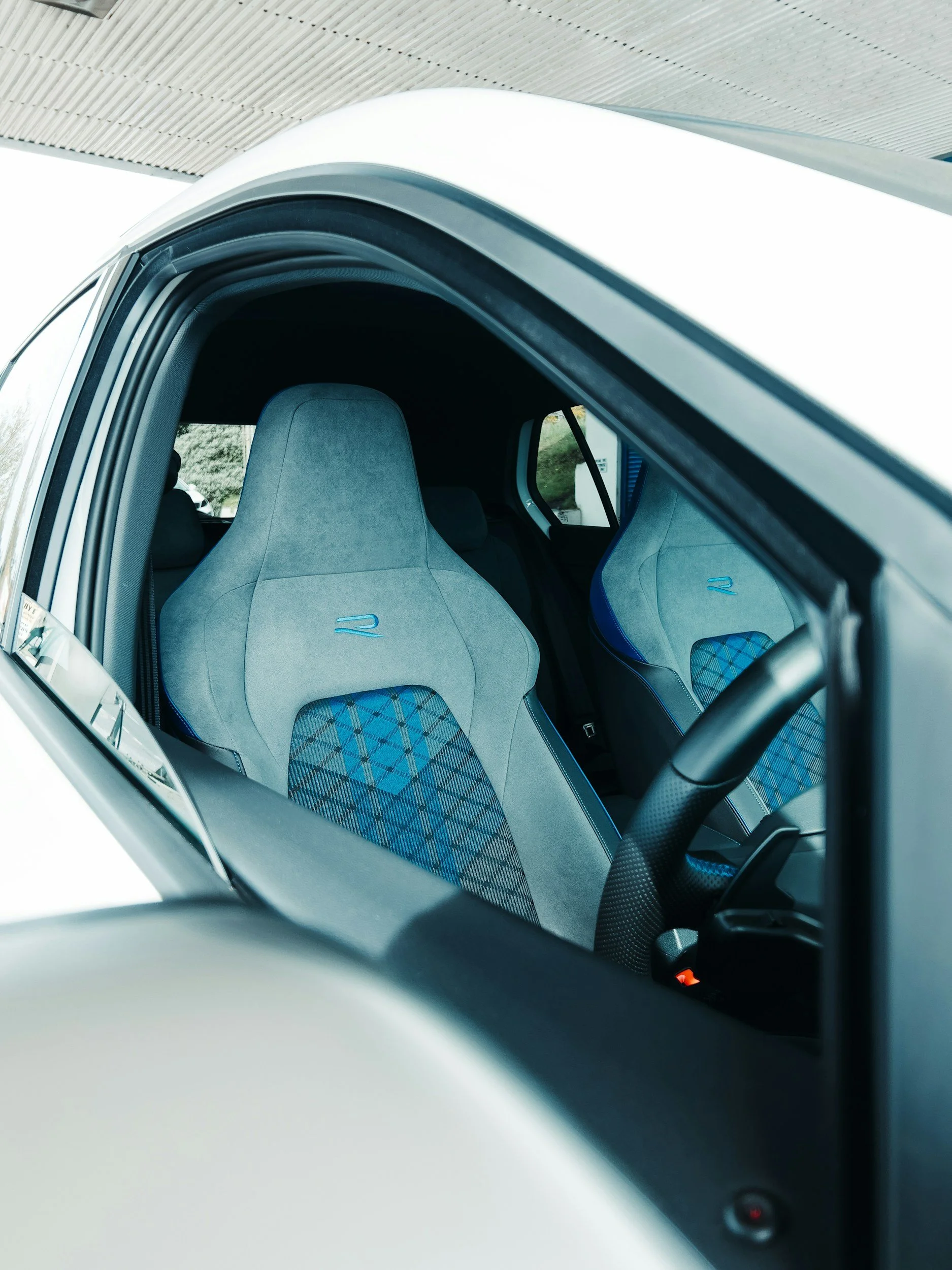 Inside an electric vehicle with gray and blue racing-style seats, viewed through the partially open driver's side window.