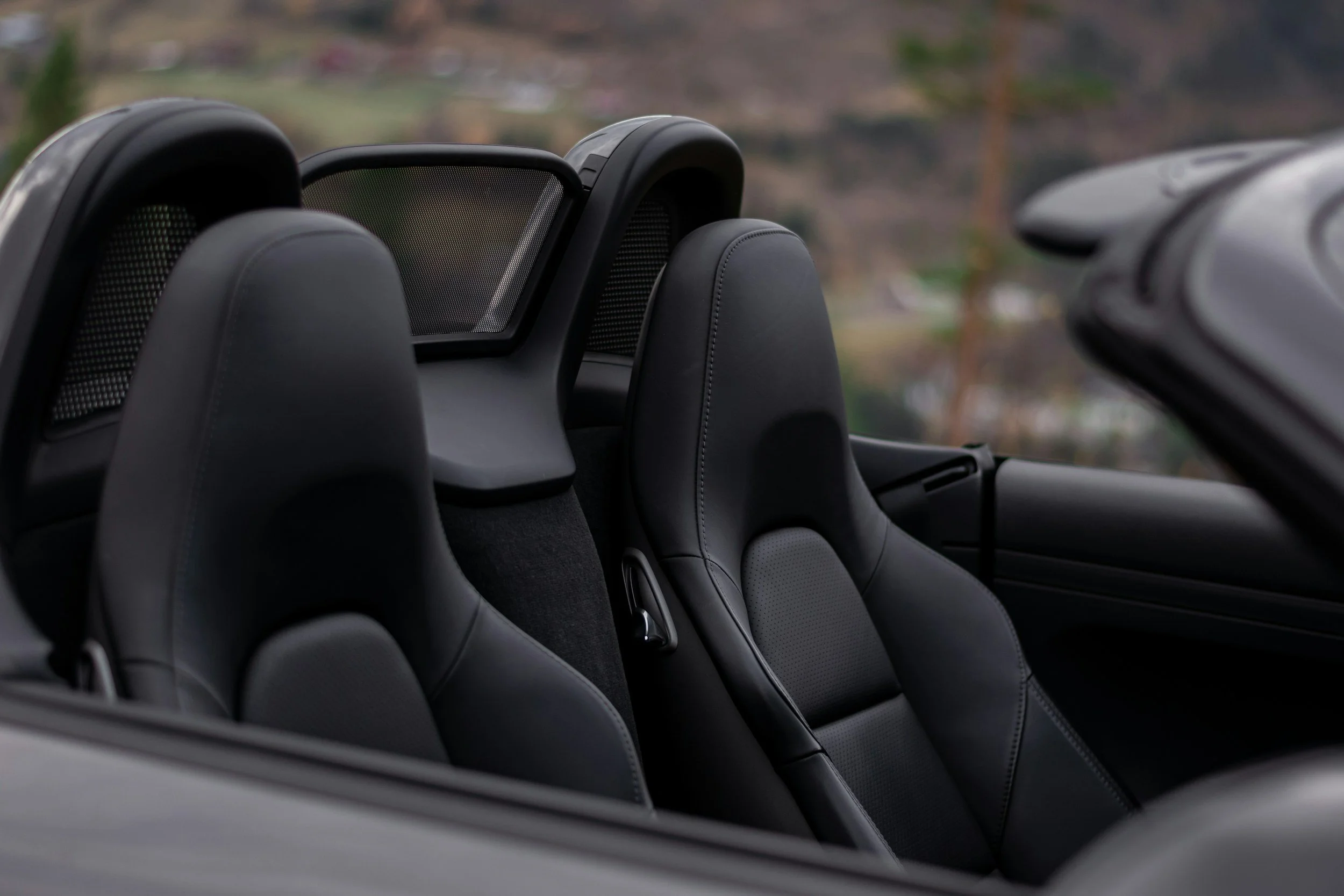Close-up view of black leather seats in a convertible car with the top down, showing the headrests and the interior side panel.