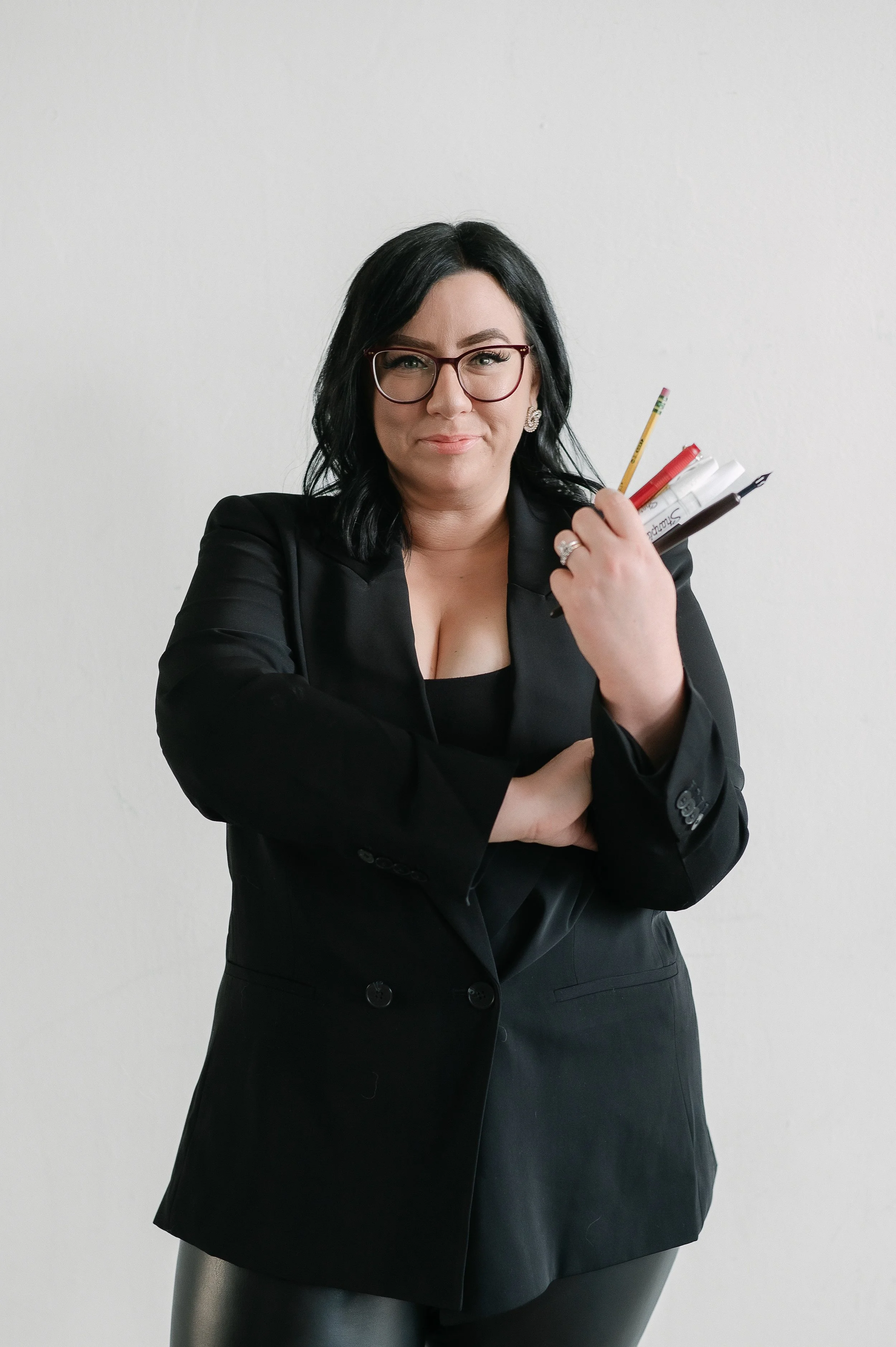 Jackie, owner of INKED by Jackie, holding calligraphy pens in a black blazer.