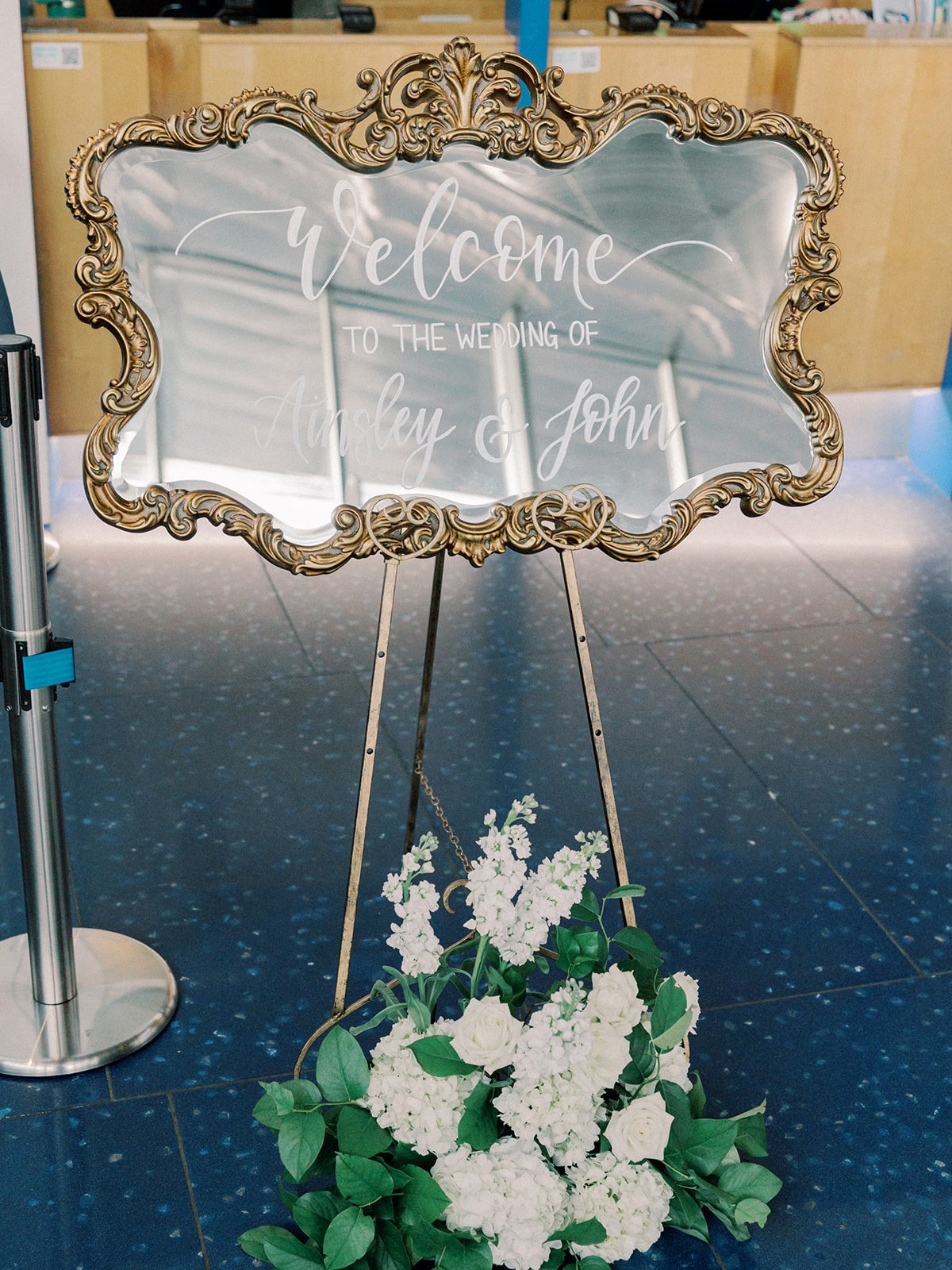 Ornate gold mirror wedding welcome sign featuring white hand-lettered calligraphy at a Boston wedding reception - New England Aquarium