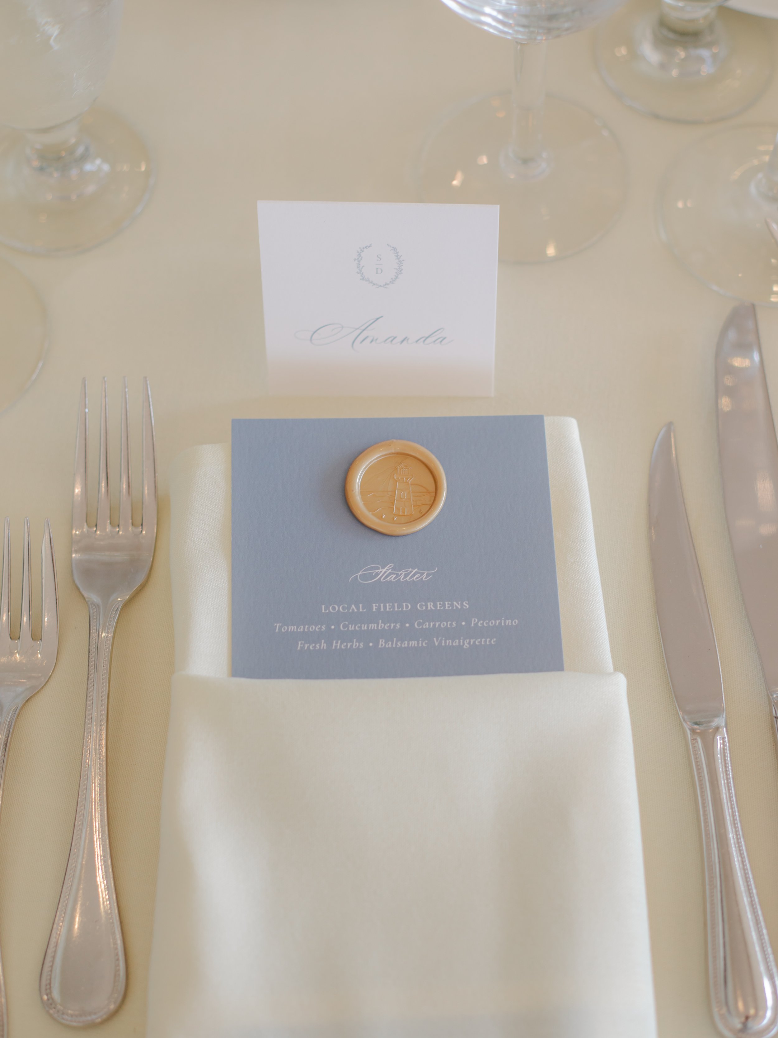 Elegant wedding table setting with a white tented place card, and dusty blue, gold wax seal menu at the OceanCliff Hotel in Newport, RI