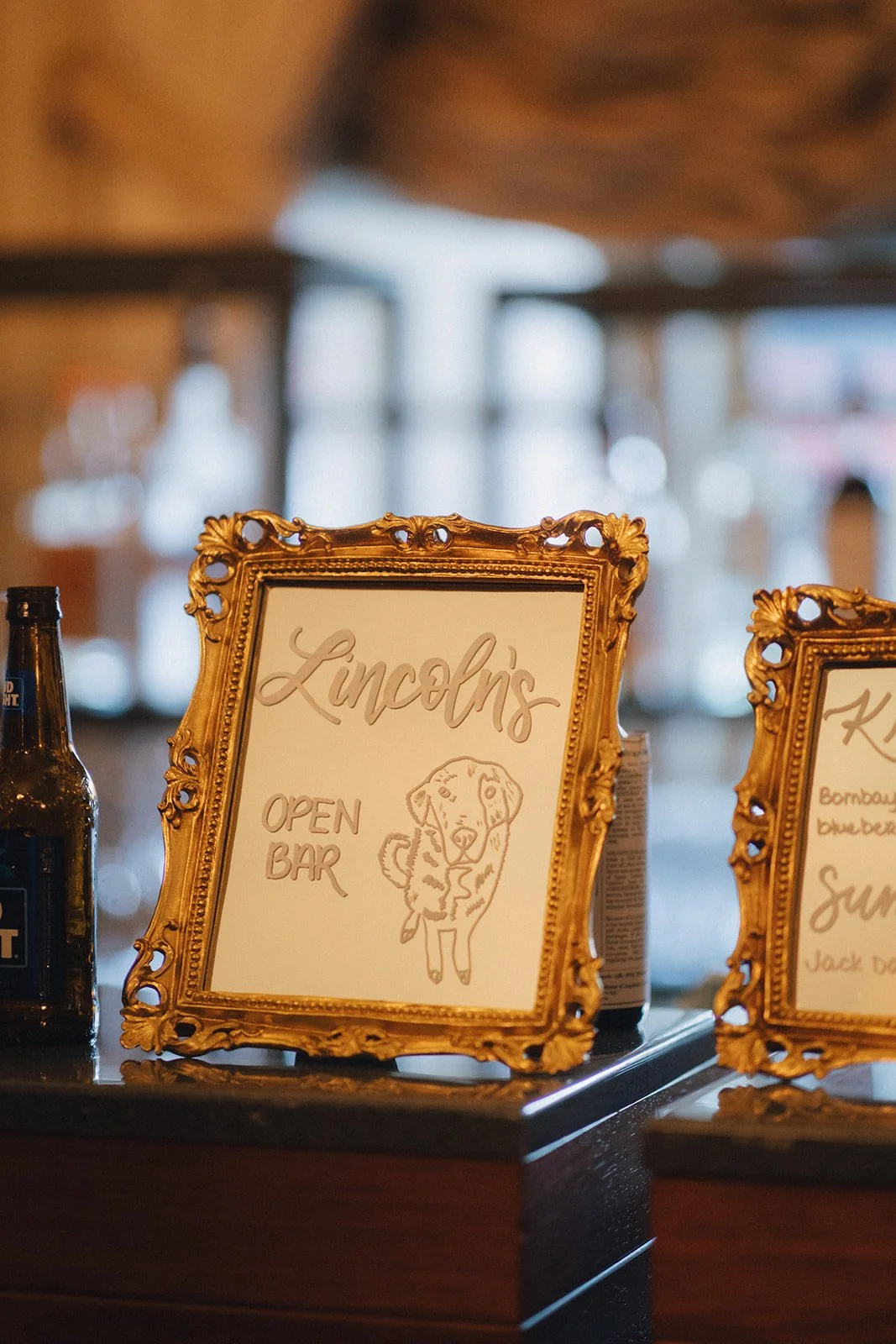 A gold ornate picture frame on a table with hand lettered "Lincoln's OPEN BAR" and a drawing of a dog