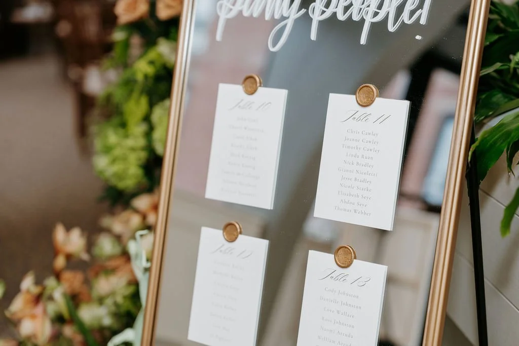 Vintage ornate gold mirror wedding seating chart featuring white hand-lettered calligraphy and card stock and wax seal - Bostonian Hotel