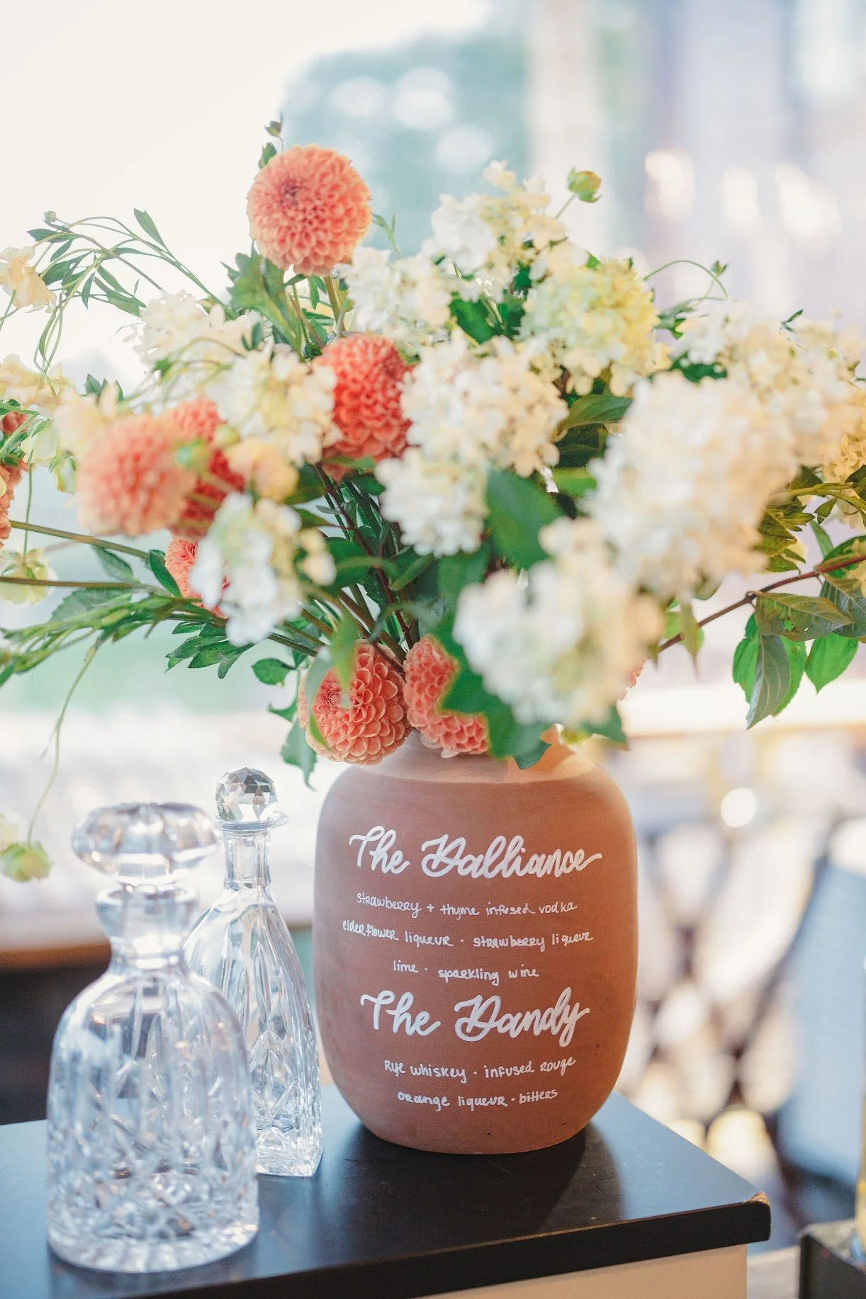 a unique, custom terra cotta pot signature cocktail sign, written in white hand-lettered calligraphy with delicate florals popping out of the top for a romantic wedding at The Barn at Gibbet Hill in Groton, MA