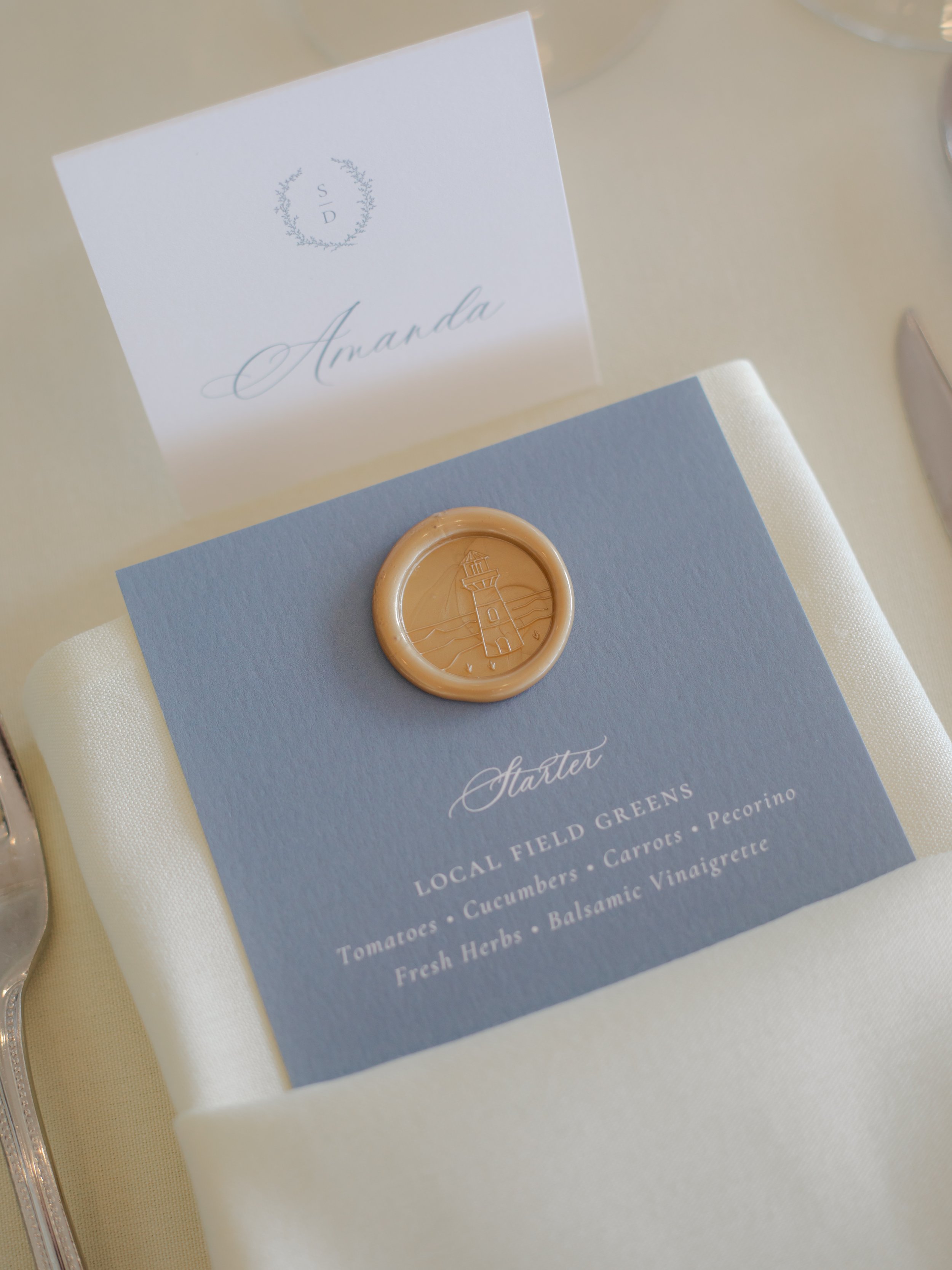 Gold wax seal and dusty blue dinner menu and place card at the OceanCliff Hotel