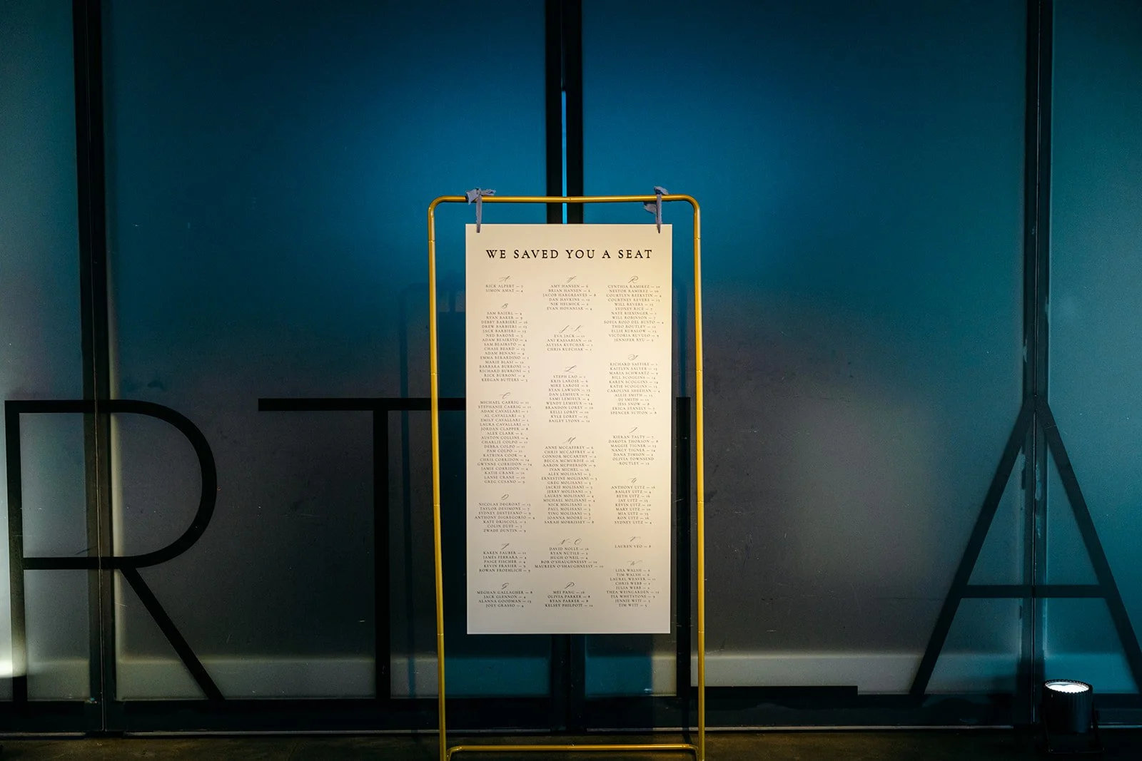 White and dusty blue acrylic seating sign, hanging on a gold metal frame at the Institute of Contemporary Arts in Boston, MA