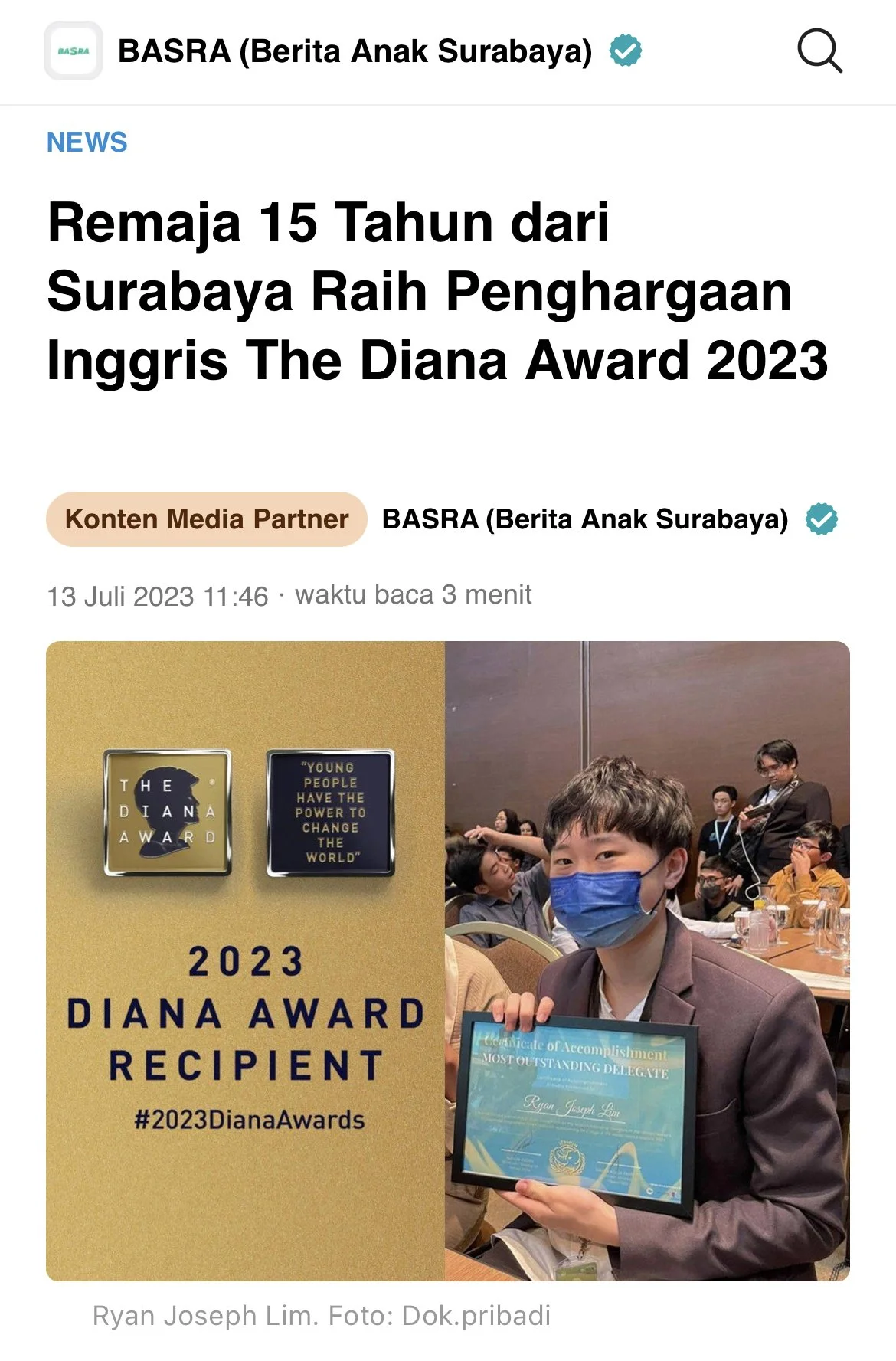 A young person wearing a blue face mask holding a framed award while sitting at a table at an event with other people.