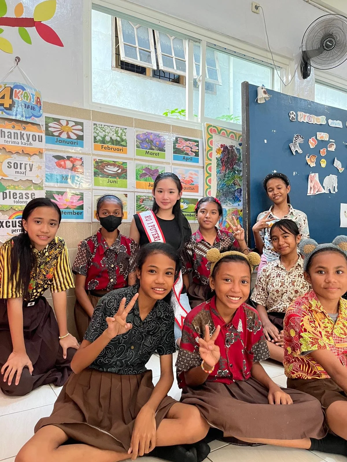 Group of schoolgirls in school uniforms posing for a photo in a classroom with colorful decorations and educational posters.