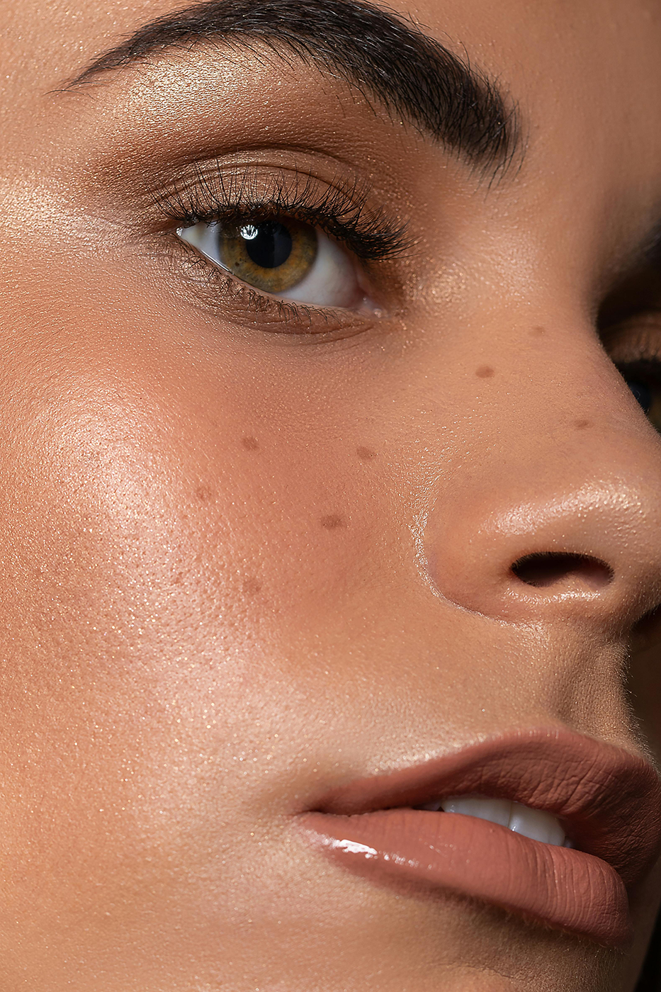Close-up of a woman's face showing her eye, nose, and lips with detailed skin texture and makeup.
