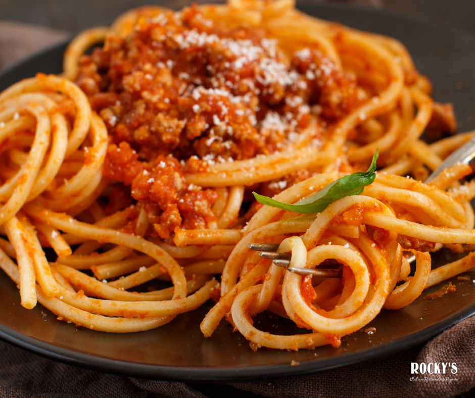 Spaghetti with marinara sauce, topped with grated cheese and a basil leaf on a black plate.