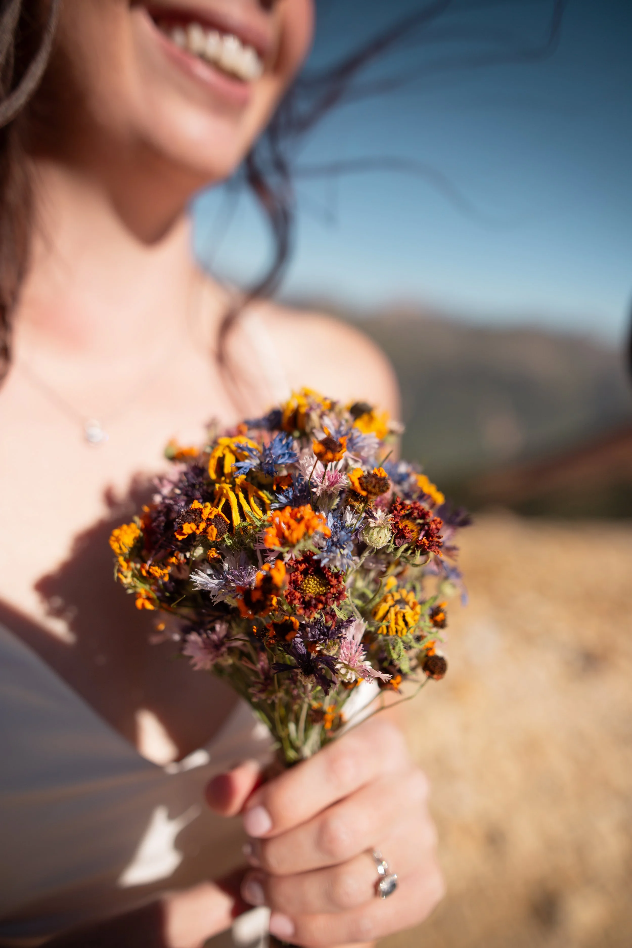 A smiling woman holding a vibrant bouquet of wildflowers outdoors on a sunny day.