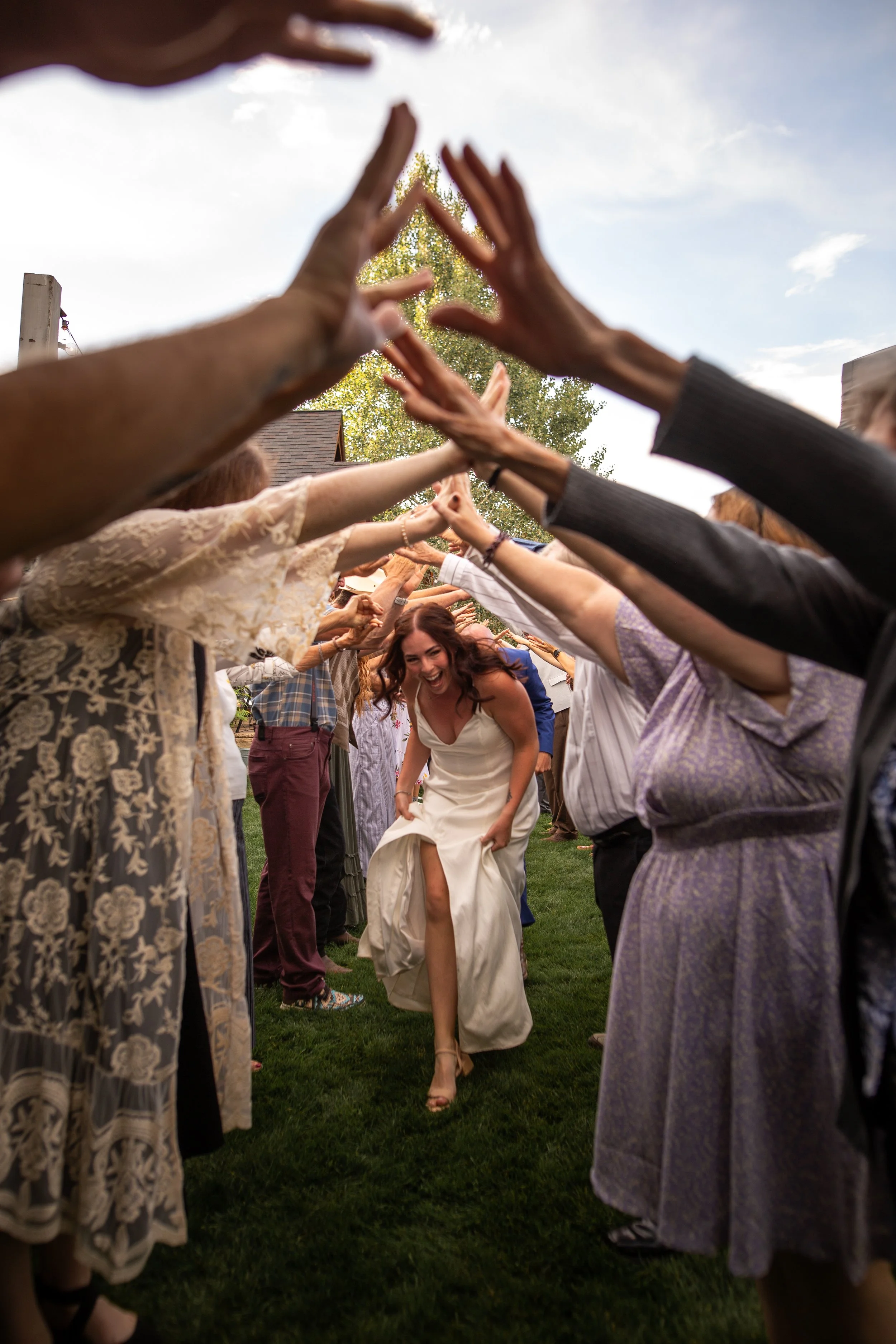 A bride walking through a tunnel of friends and family forming an arch with their arms during a wedding celebration outdoors.