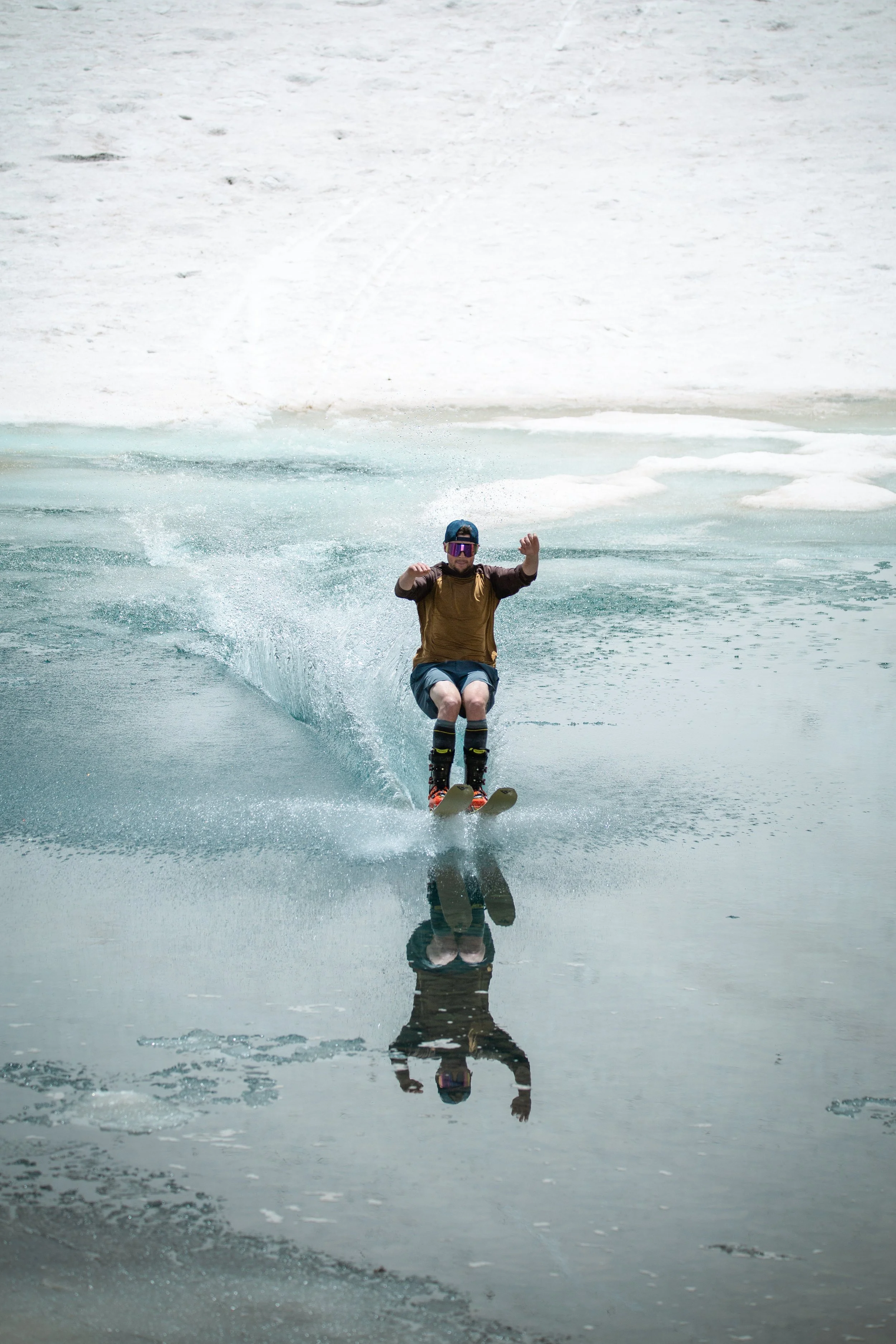 Person wakeboarding on a partially frozen lake with snow-covered terrain in the background.