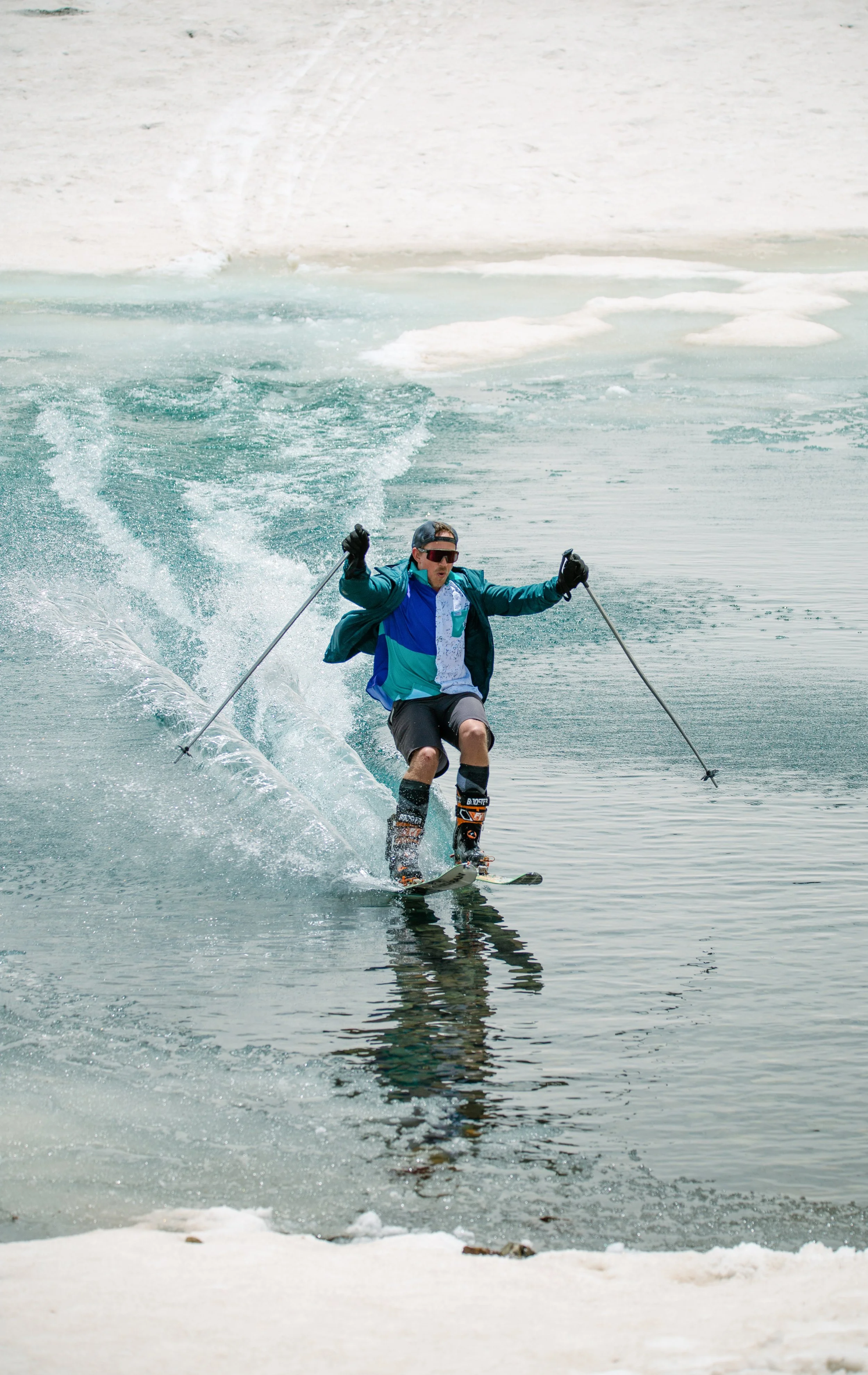 Man skiing on a water body (pond skimming) with snow and ice in the background.
