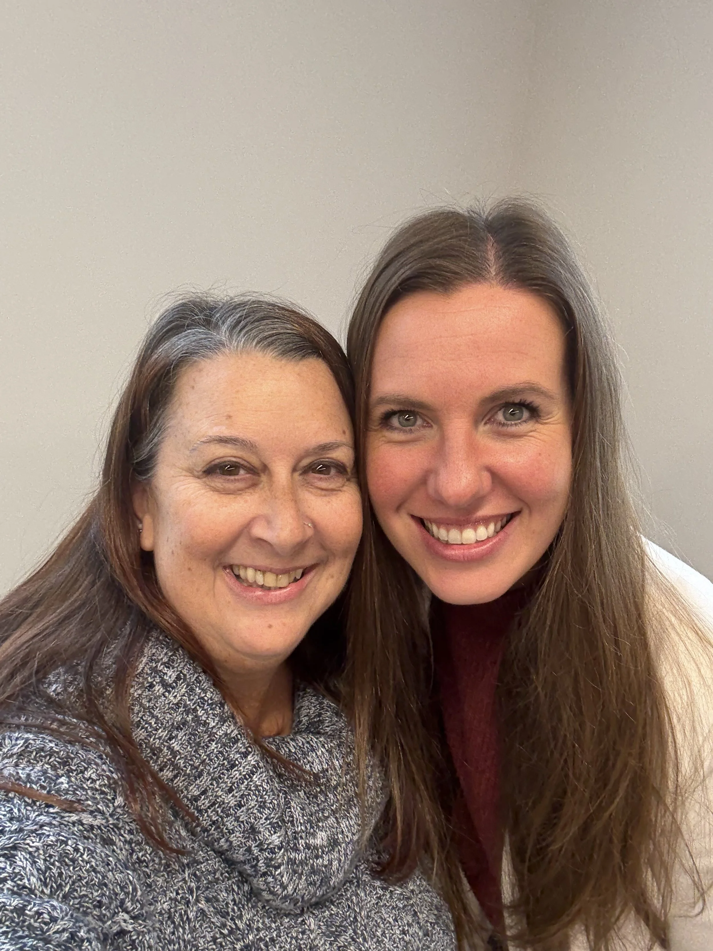 Two women smiling, close up portrait, plain background.