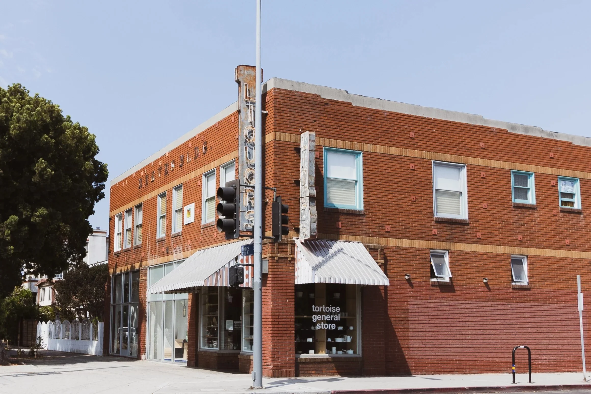 A three-story brick building with large windows, a metal awning over the entrance, and a vertical sign that reads 'LOFTS'. The store window displays the text 'tortoise general store'. There are traffic lights and a street sign at the corner, and a la