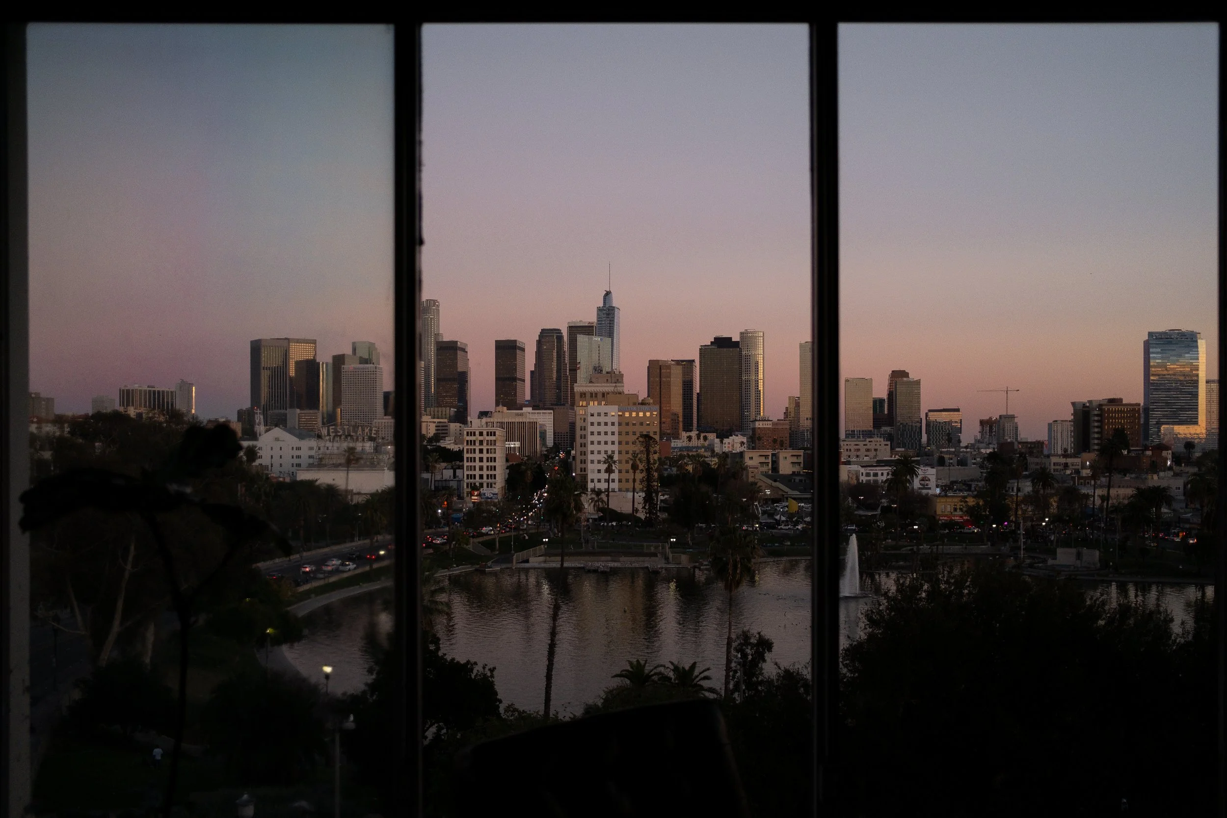 View of downtown Los Angeles skyline at dusk, seen through large window panes.