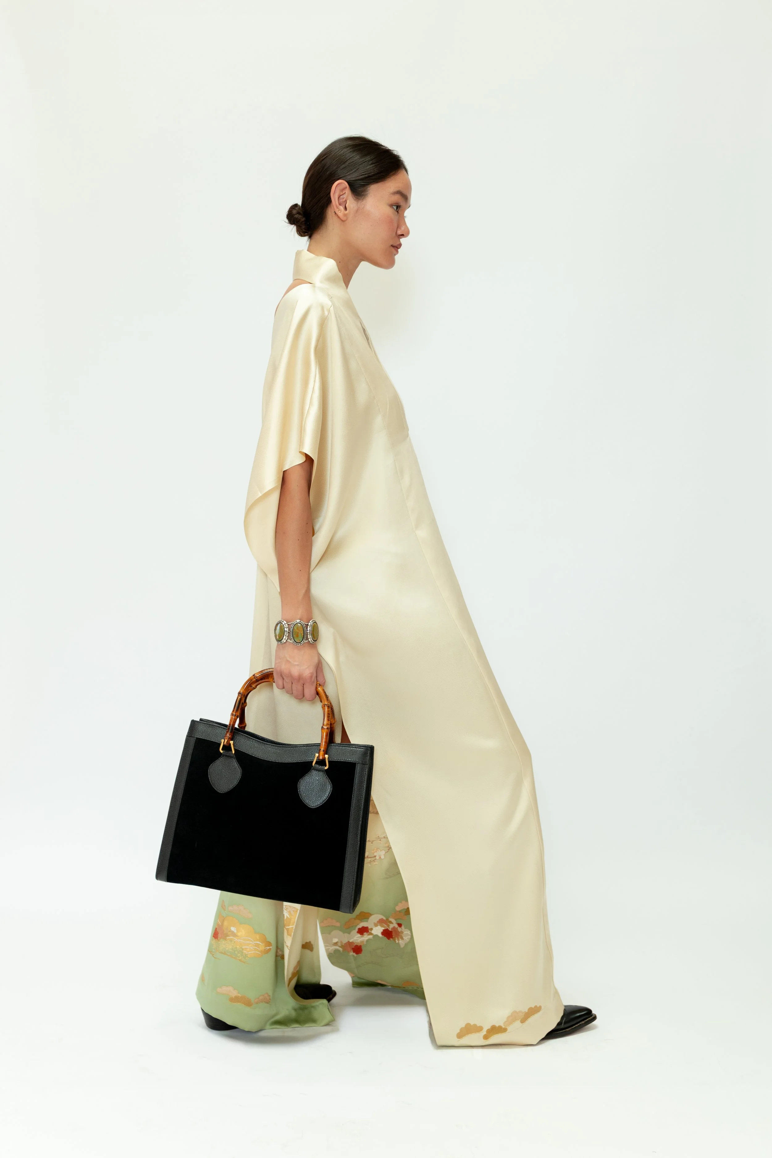 Woman dressed in traditional Japanese kimono holding a black handbag with bamboo handles, standing sideways against a plain white background.