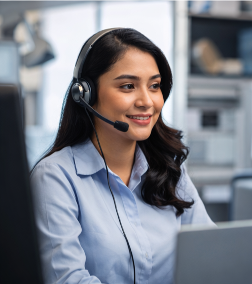 Young woman wearing a headset and blue shirt working at a computer in an office